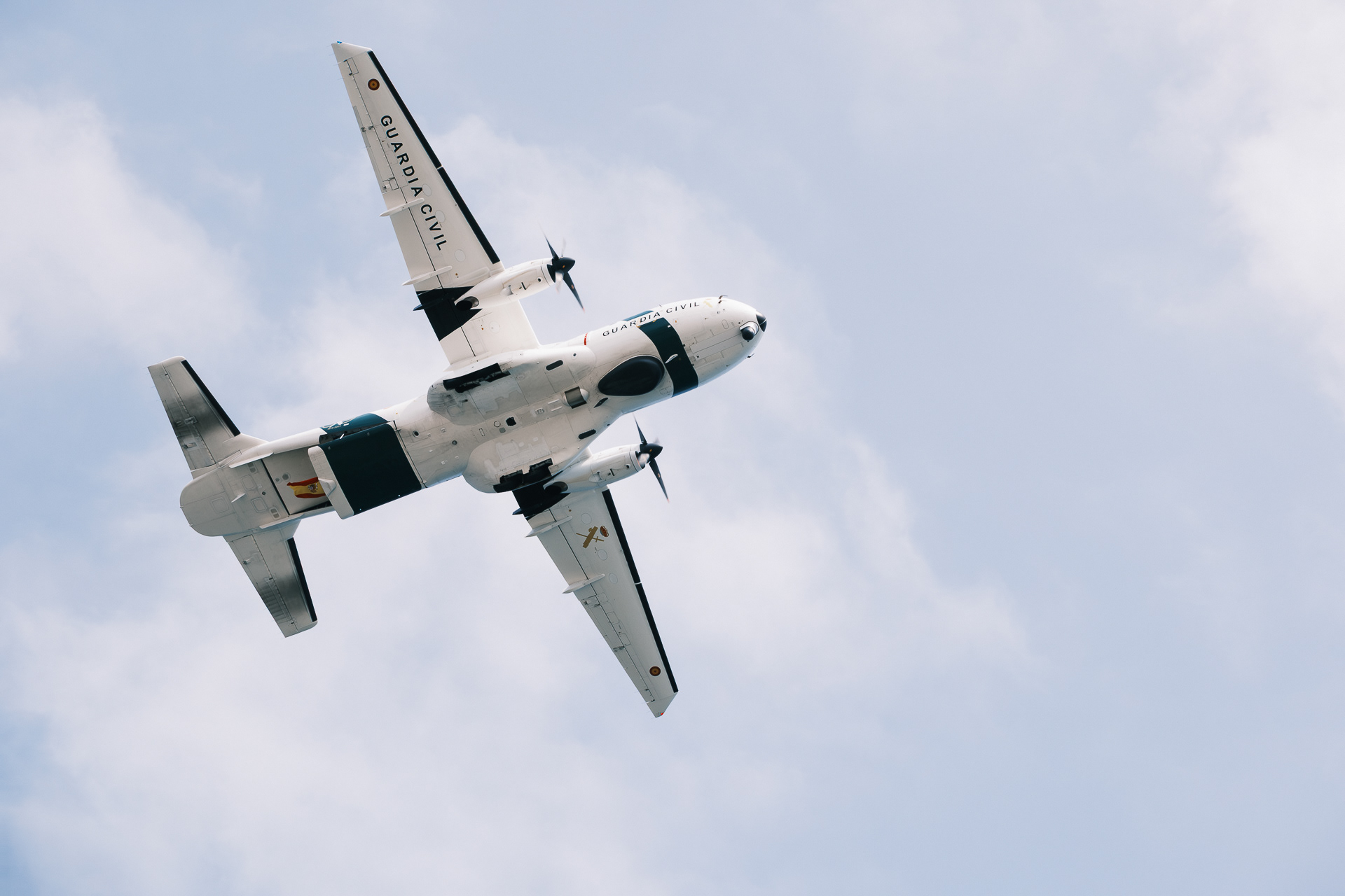 Avión bimotor de la Guardia Civil visto desde abajo entre nubes.