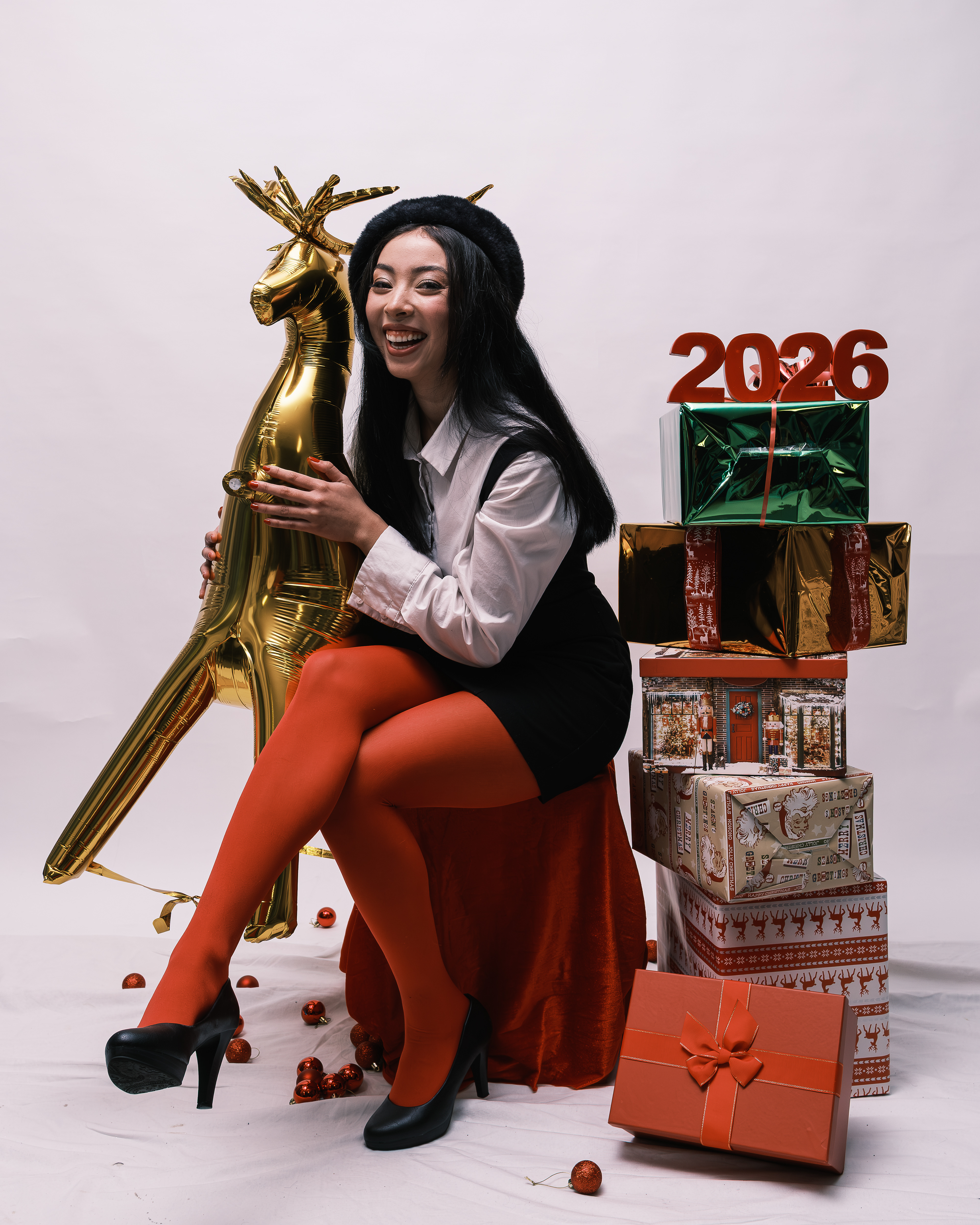 Mujer sonriente sentada junto a un reno dorado y una pila de regalos de Navidad.