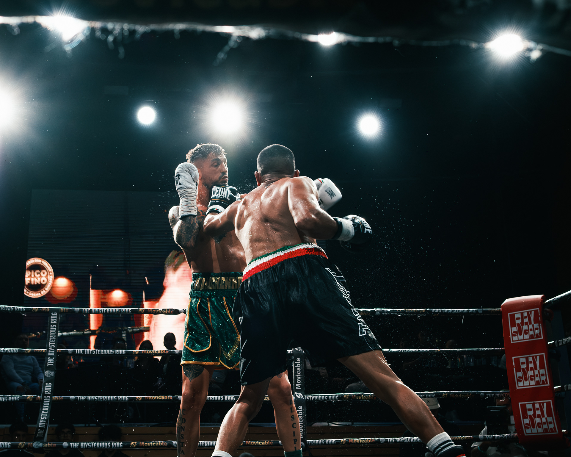 Dos boxeadores profesionales intercambiando golpes bajo los focos del ring.