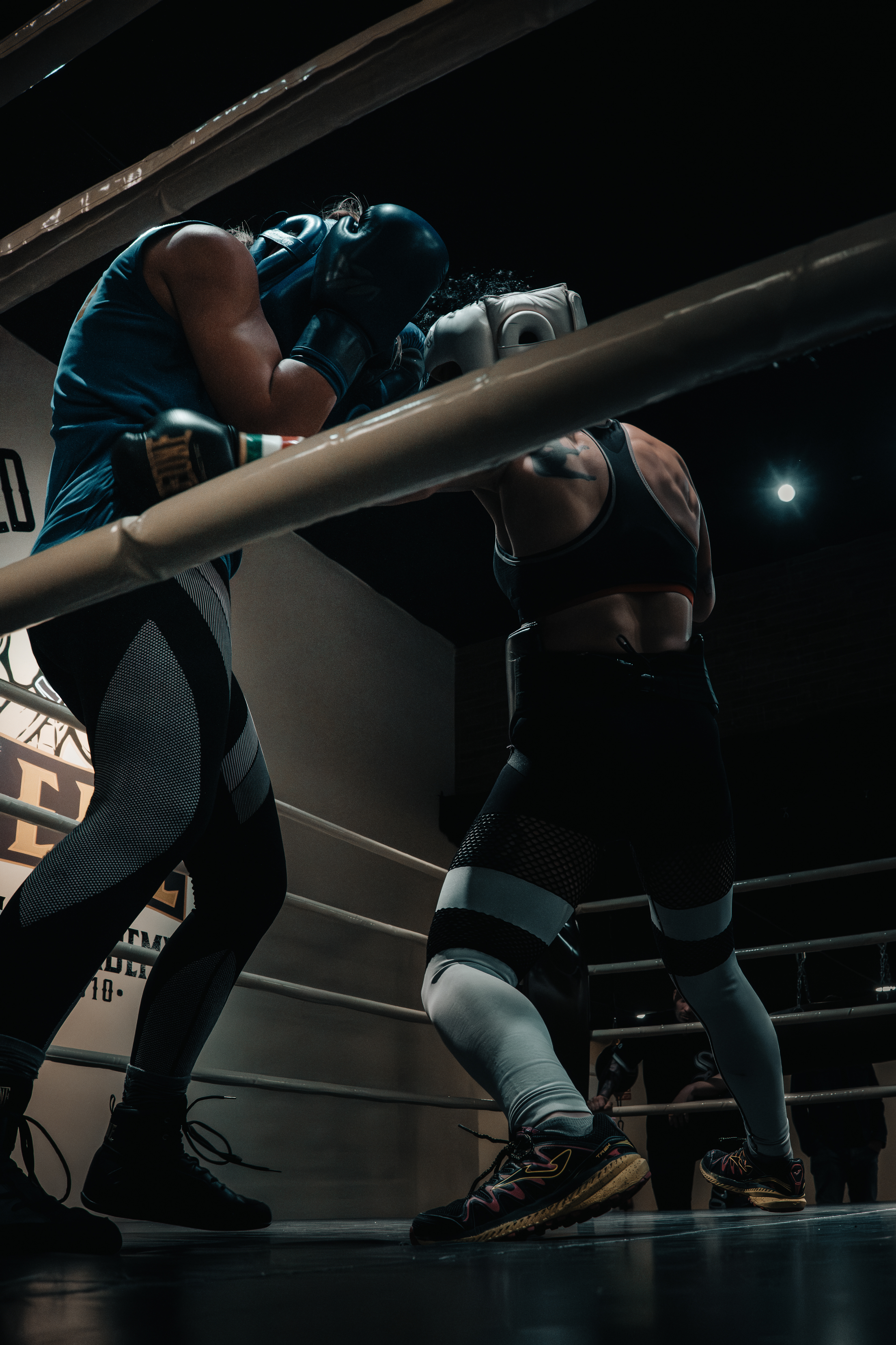 Dos boxeadoras con cascos azul y blanco entrenando cerca de las cuerdas del ring.