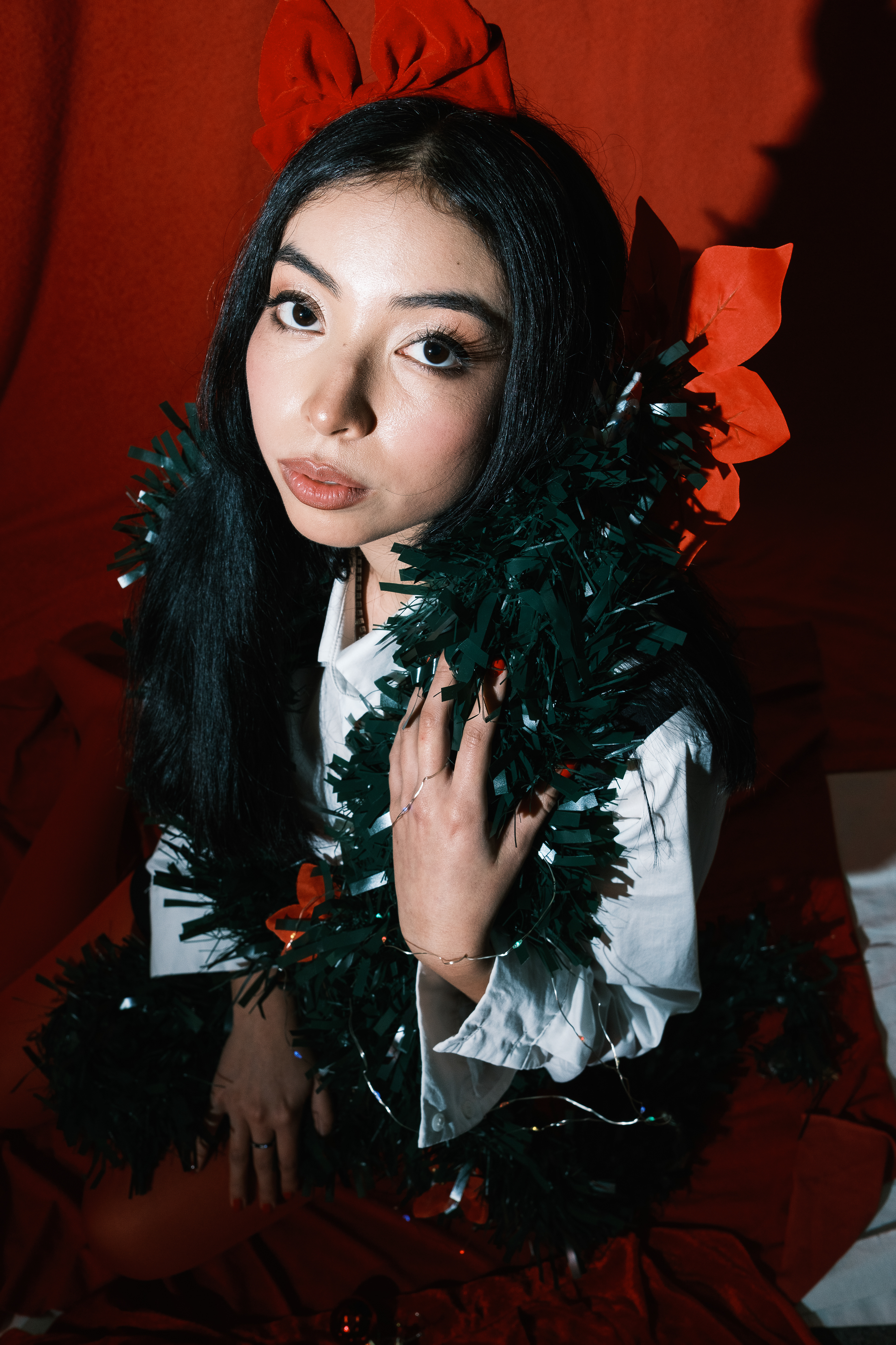 Mujer sentada con vestido rojo, sosteniendo una gran esfera navideña entre regalos.