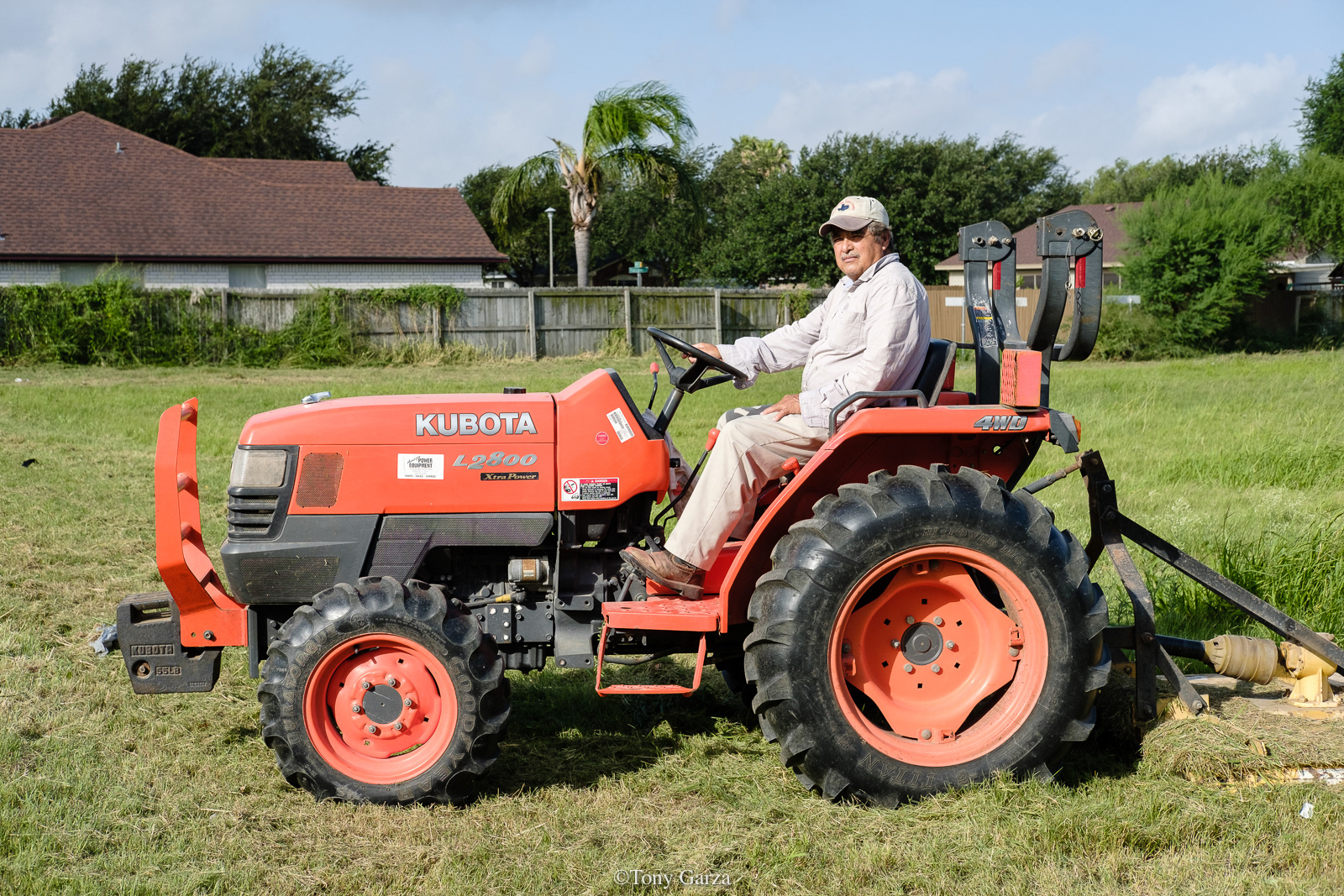 An elderly man mows grass with a tractor, McAllen, Texas, July 2020.