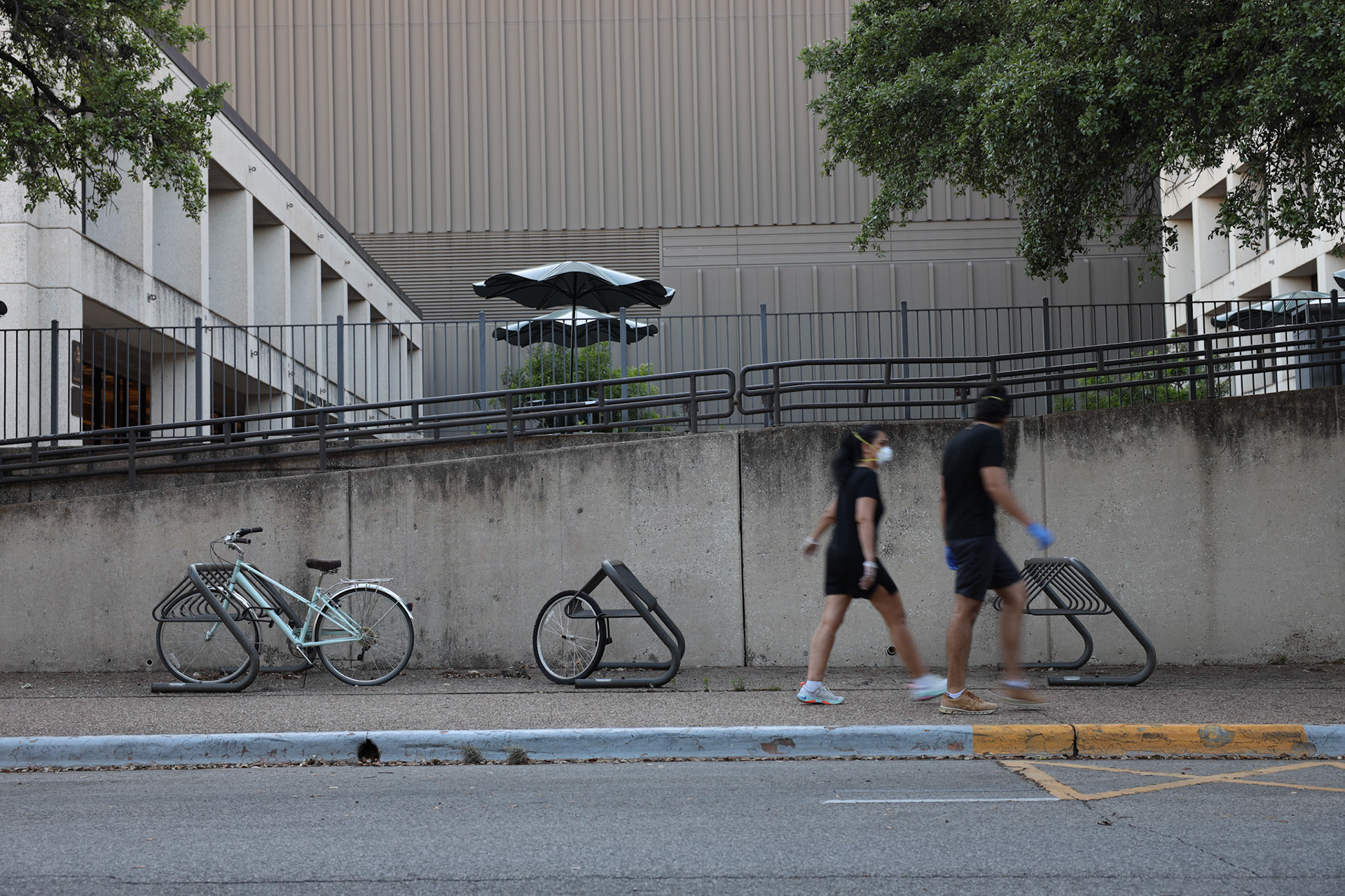 Two young adults walk by an empty bike rack and communications building at The University of Texas at Austin on April 19, 2020. UT Austin moved to online classes after spring break to safely continue instruction.