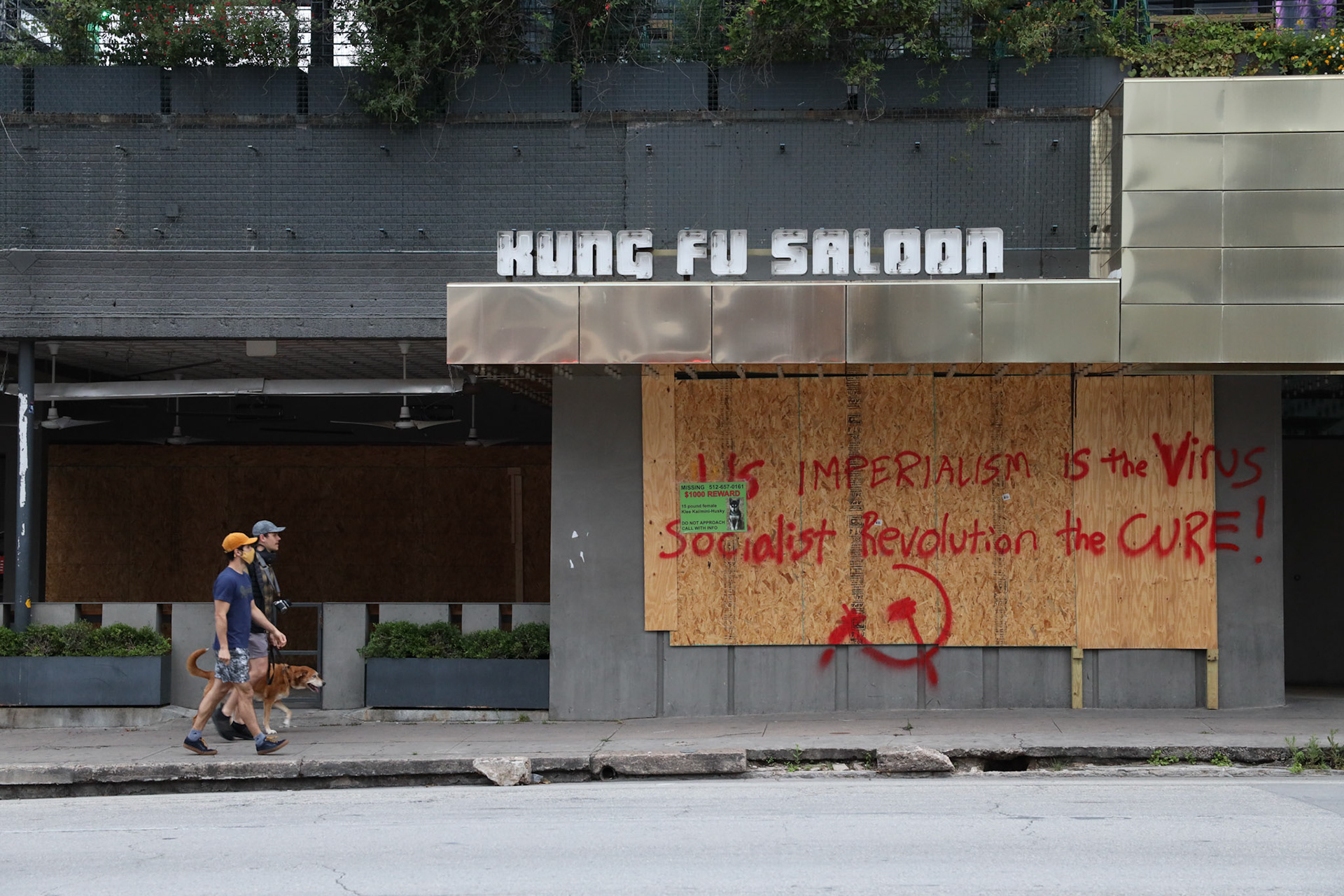 Two men walk their dog by the tagged up Kung Fu Saloon on April 18, 2020