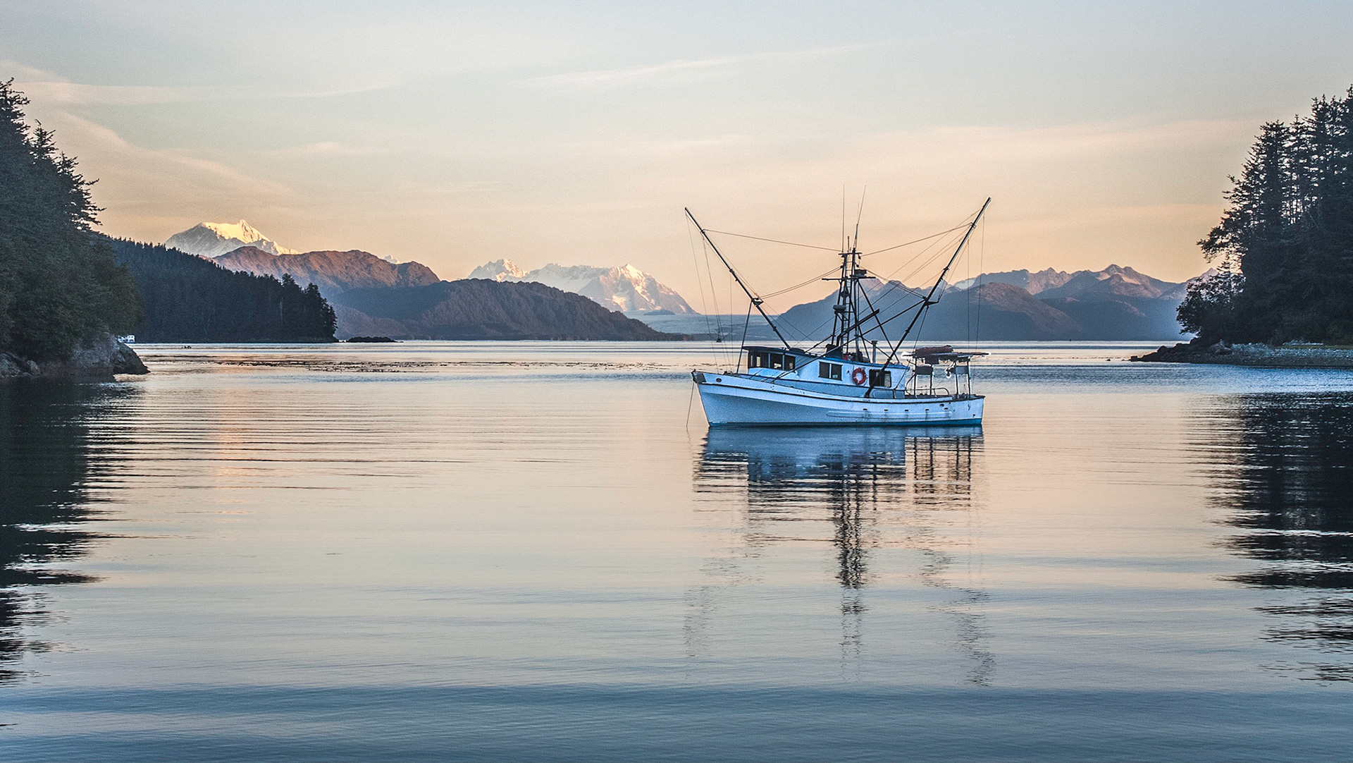 A fishing boat waits in Mite Cove, Alaska with Glacier National Park in the background.