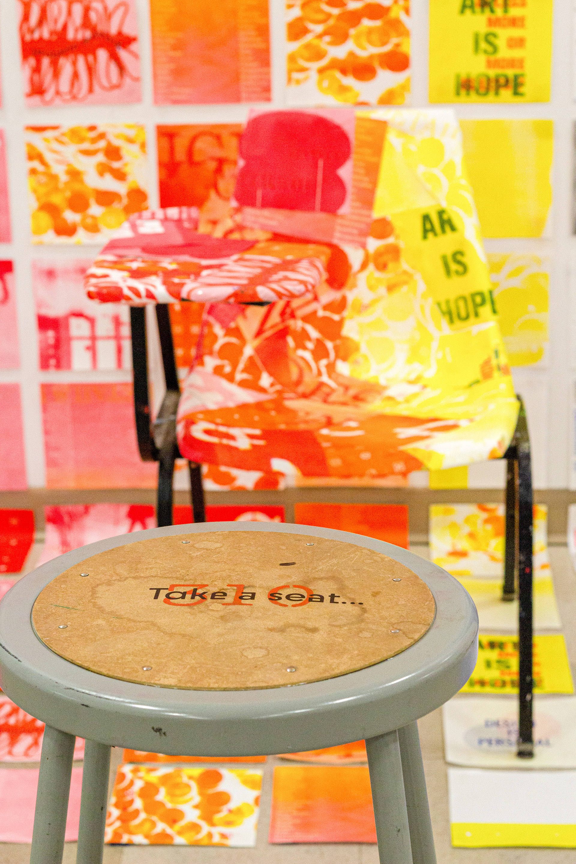 Detail. Black vinyl text on stool. Desk chair covered in risograph prints.