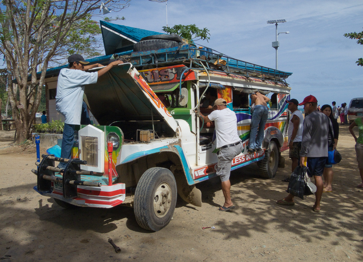 Driver checking under bonnet as passengers boars his jeepney at Sabang, Palawan, Philippines, 2009