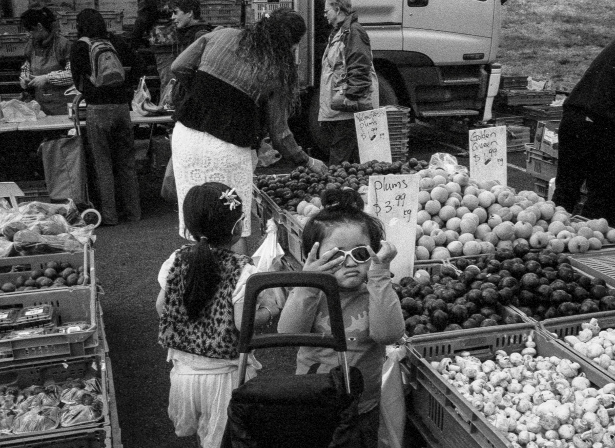 Girl with sunglasses amongst vegetable stalls, Riverbank market, Lower Hutt, 2016