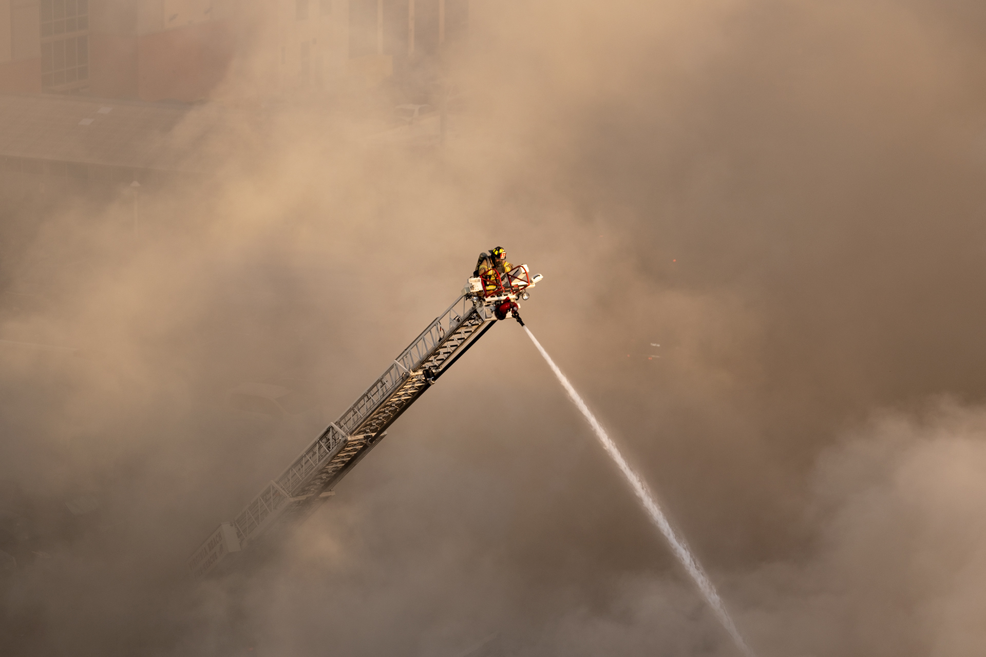 A firefighter controls a hose from the top of a ladder as the Virginia Beach fire department work a fire in the 2600 block of Atlantic Avenue at the Virginia Beach oceanfront, July 11, 2023.