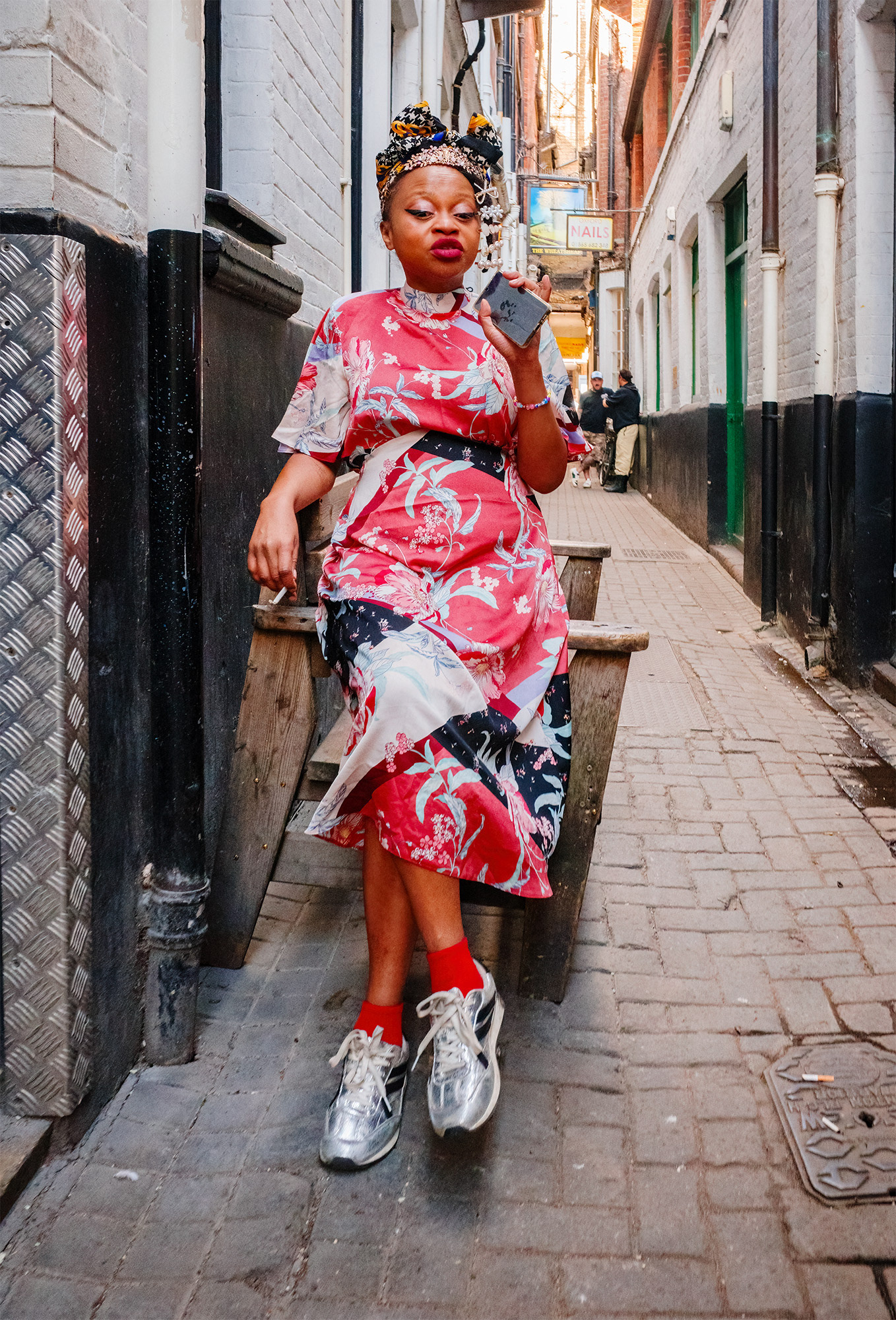 Black lady in red, white and black silk dress and headdress, smoking in an Oxford alleyway