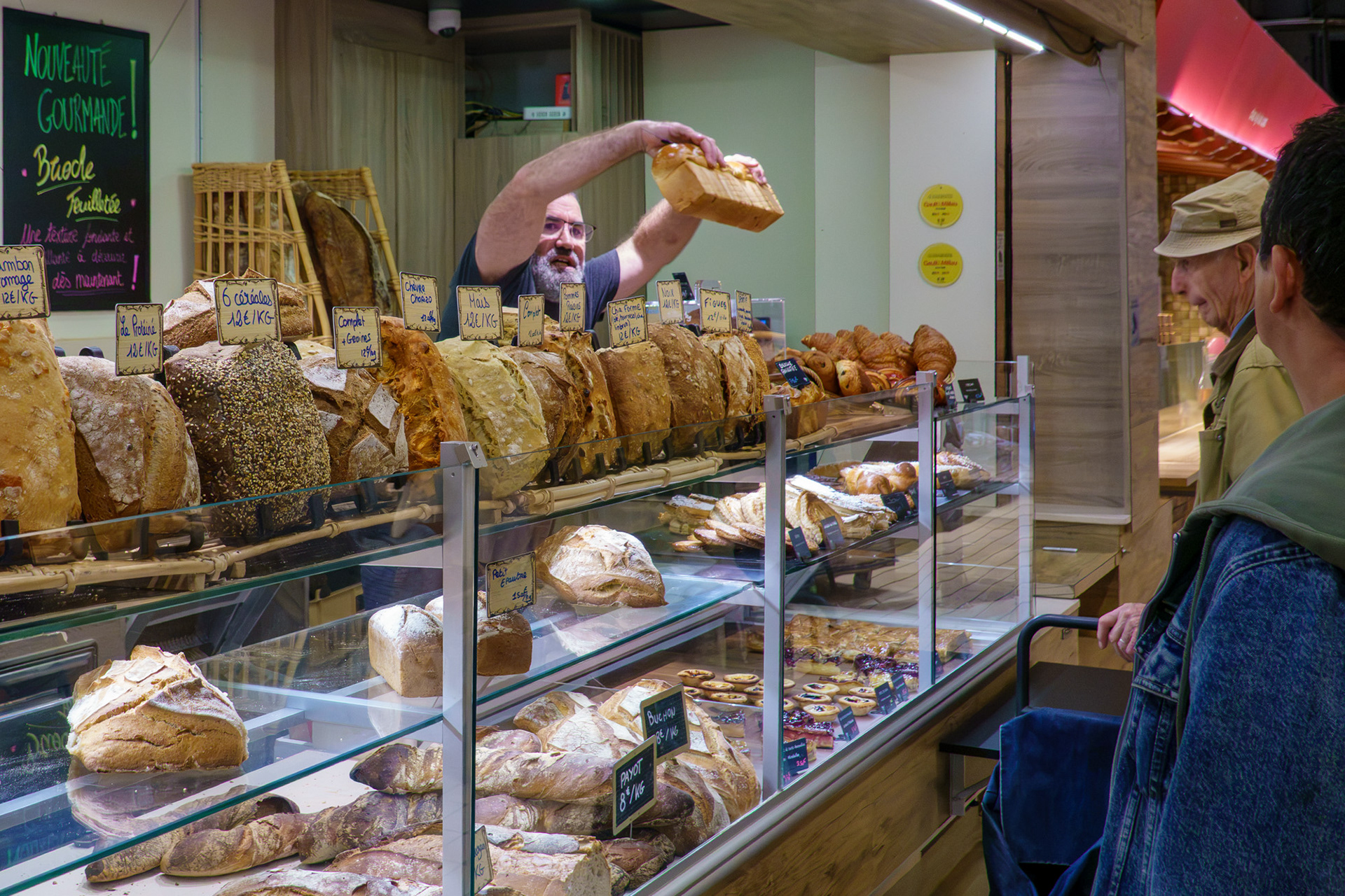 A baker in Lautrec, France, behind a long row of loaves holds one up high for customer approval 
