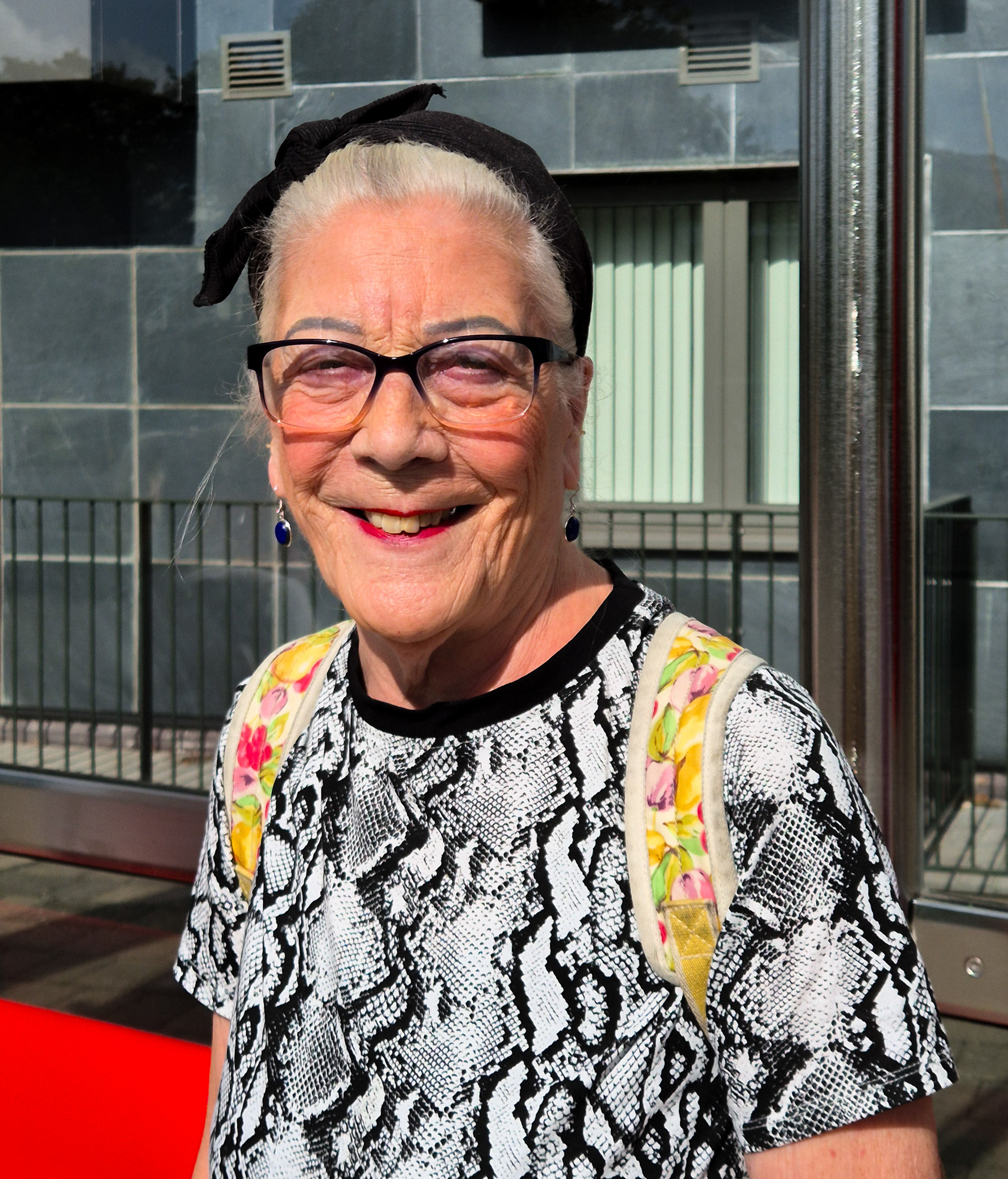 White older lady with black headdress, bright lipstick and animal print t-shirt at Bristol bus stop