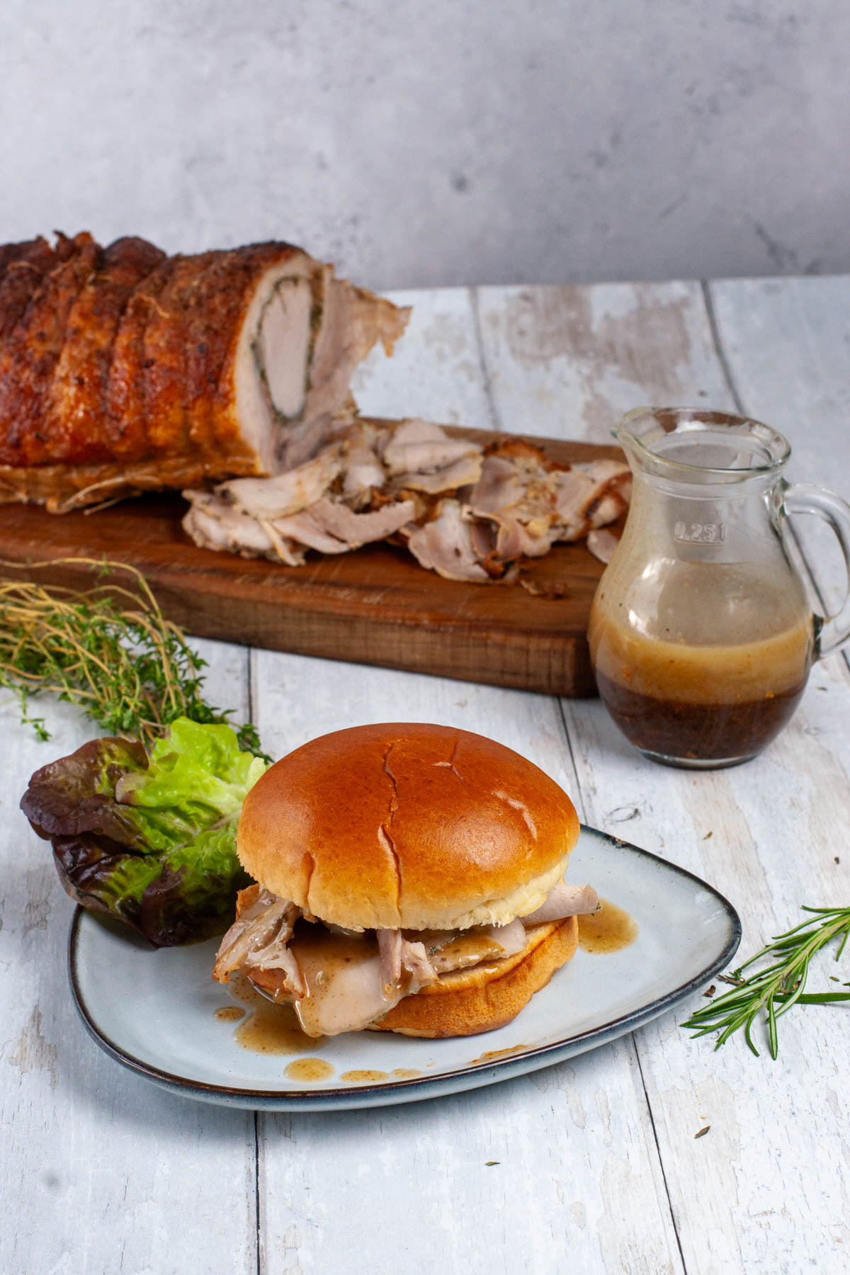 Porchetta Romana sandwich and gravy, with a sliced roasted porchetta roll in the background.