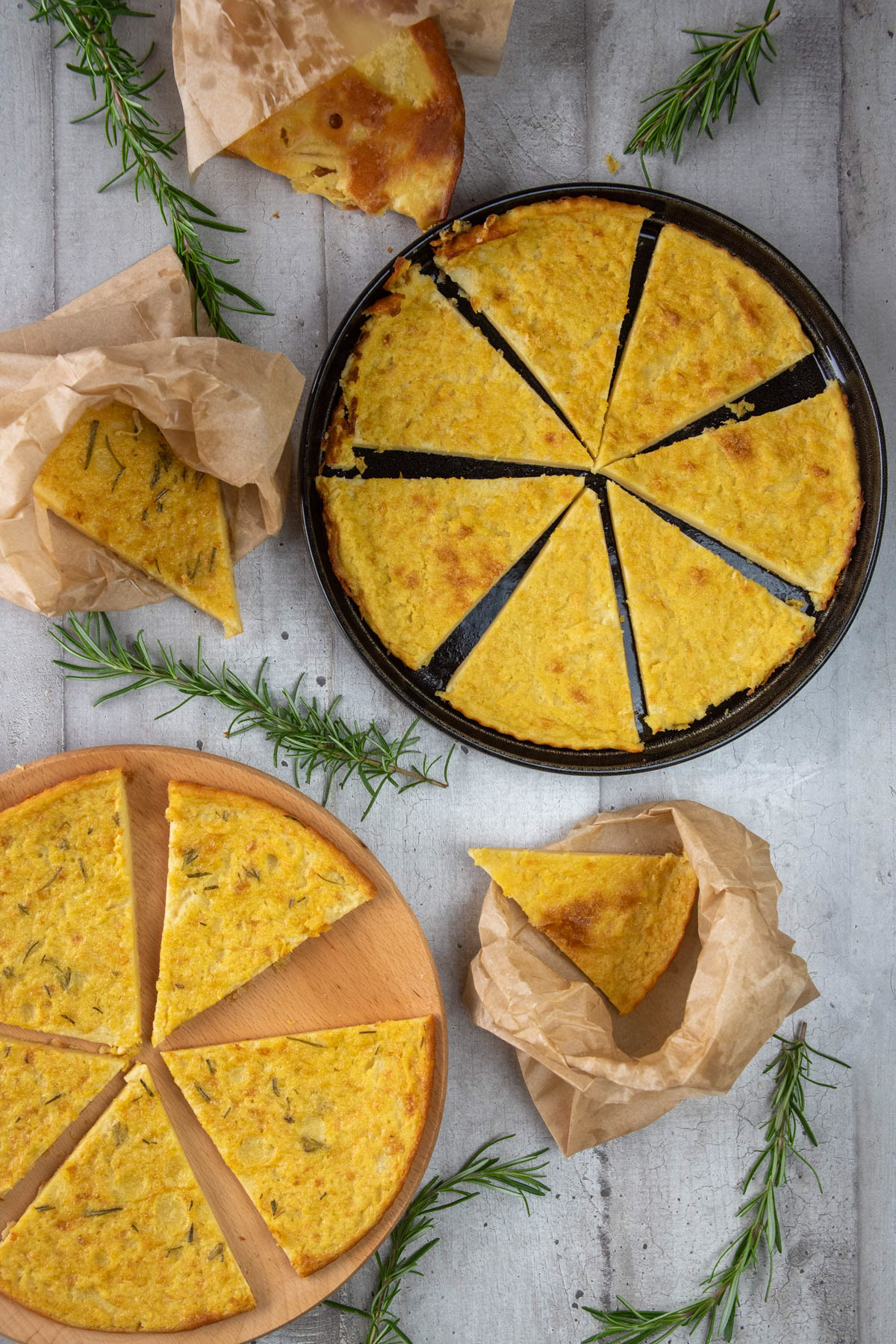 Sliced farinata in a black pan and on a wooden board with fresh rosemary.