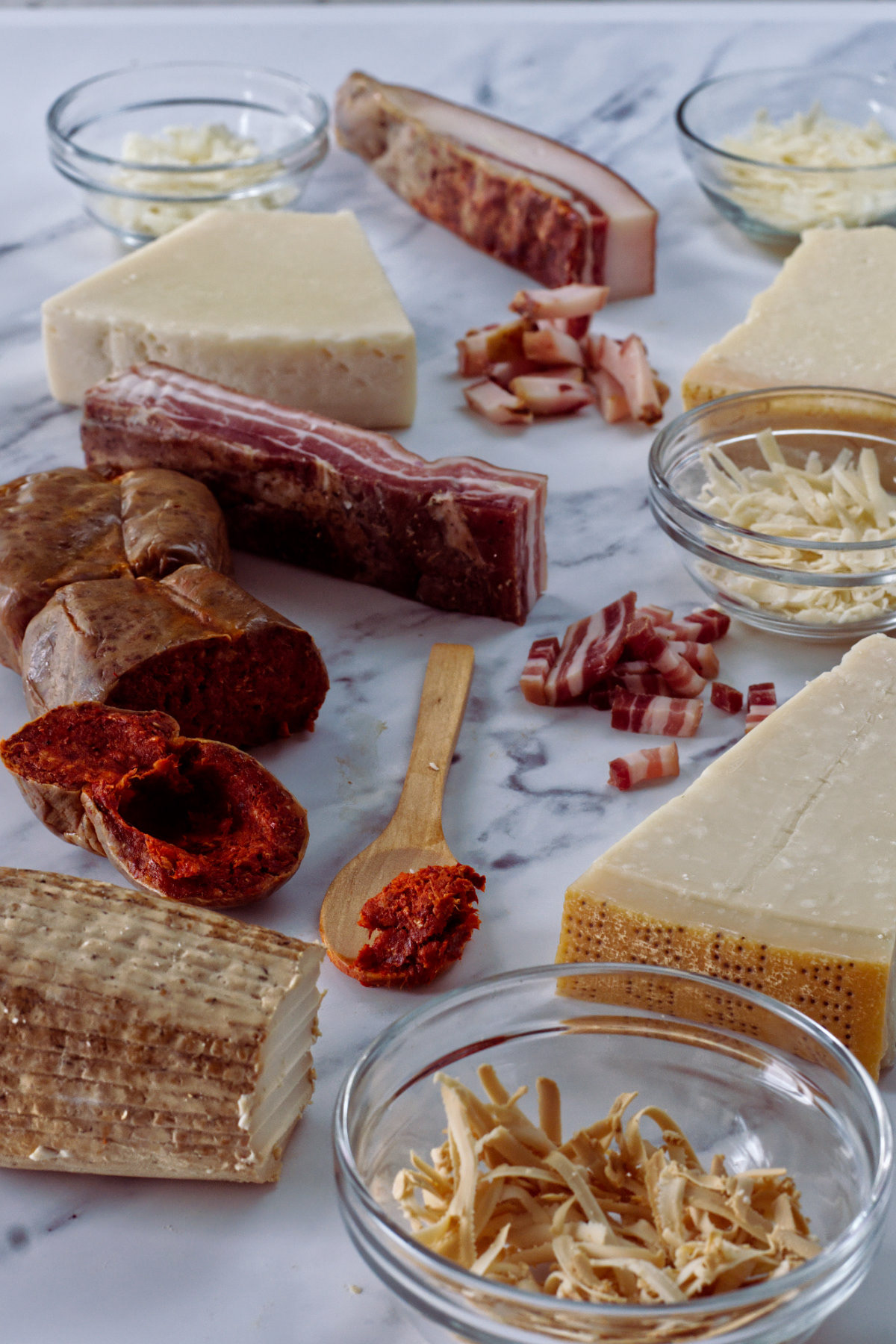 An assortment of Parmigiano, Pecorino, Grana Padano, and Ricotta Salata cheeses with pancetta, guanciale, and 'nduja on marble.