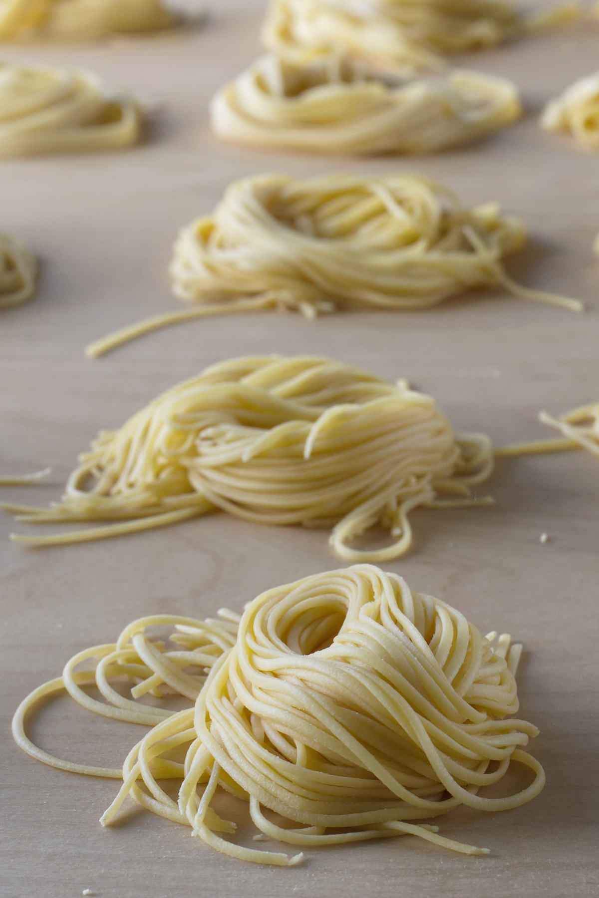 Close-up of freshly shaped raw pasta nests arranged in rows on a light wooden work surface.