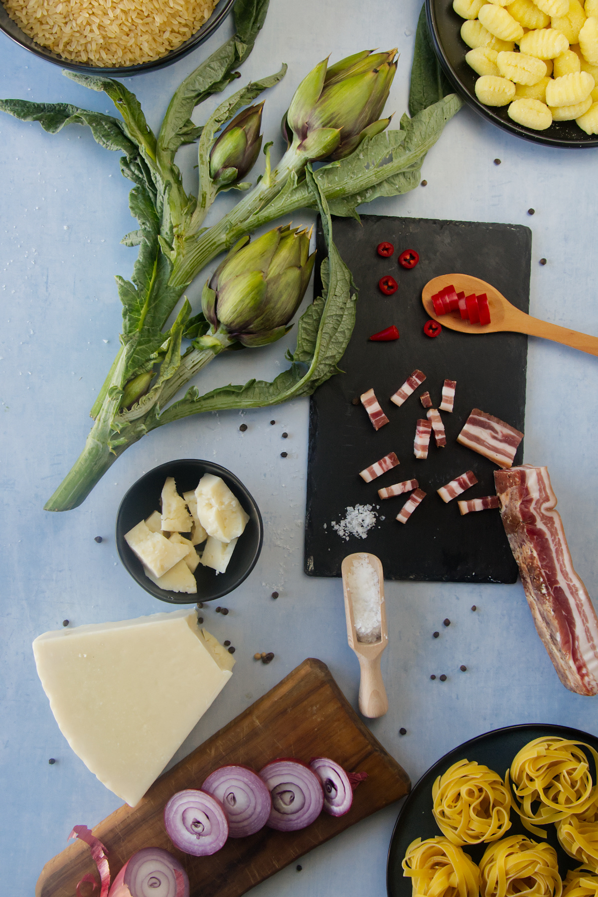 Assorted fresh Italian ingredients including sliced red onions, gnocchi, and chili peppers arranged for a recipe.