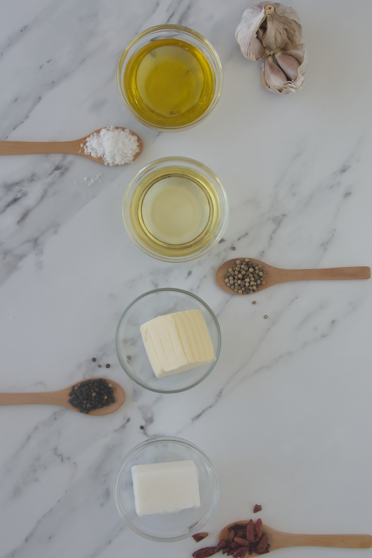 Essential pantry staples including olive oil, butter, lard, garlic, sea salt, black and white peppercorns, and dried chili peppers.