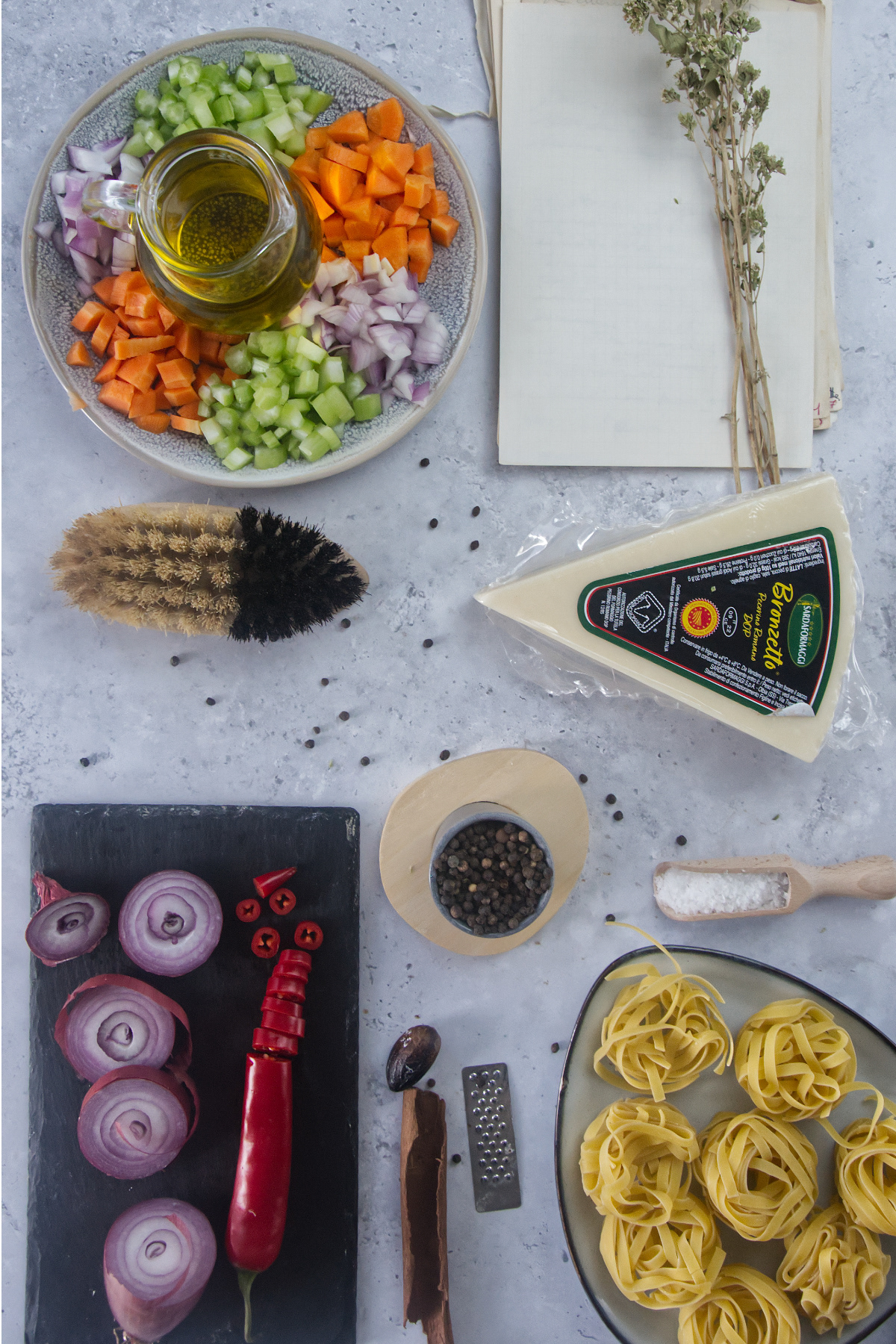 Overhead view of cooking ingredients including chopped vegetables, Pecorino cheese, pasta nests, and spices.