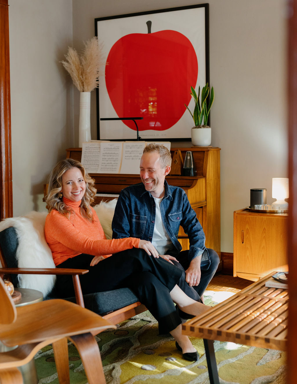 Gwen and Ryan sitting in a cozy living room with a large print of an apple hanging on the wall behind them.