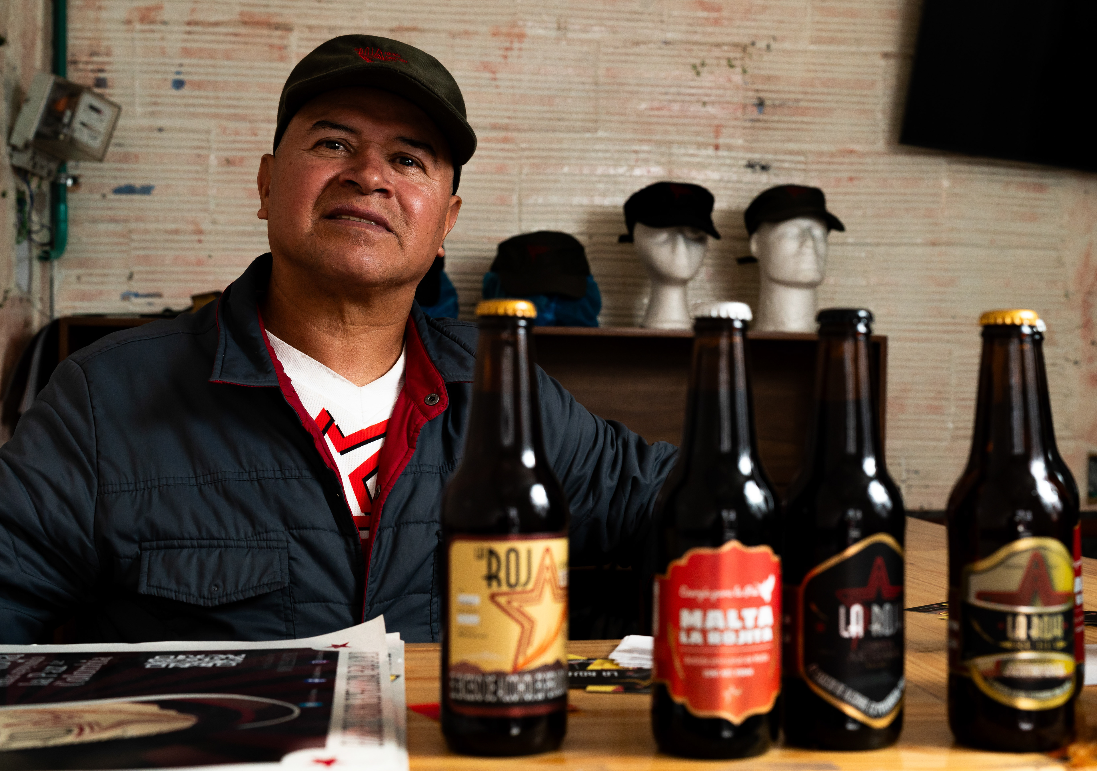 Rubén Dario Jaramillo Cardona, a firmante and brewer of Cerveza La Roja, poses for a portrait with some of the firmante-run beer brand's products in the Barrios Unidos neighborhood of Bogotá, Colombia on March 18, 2024.