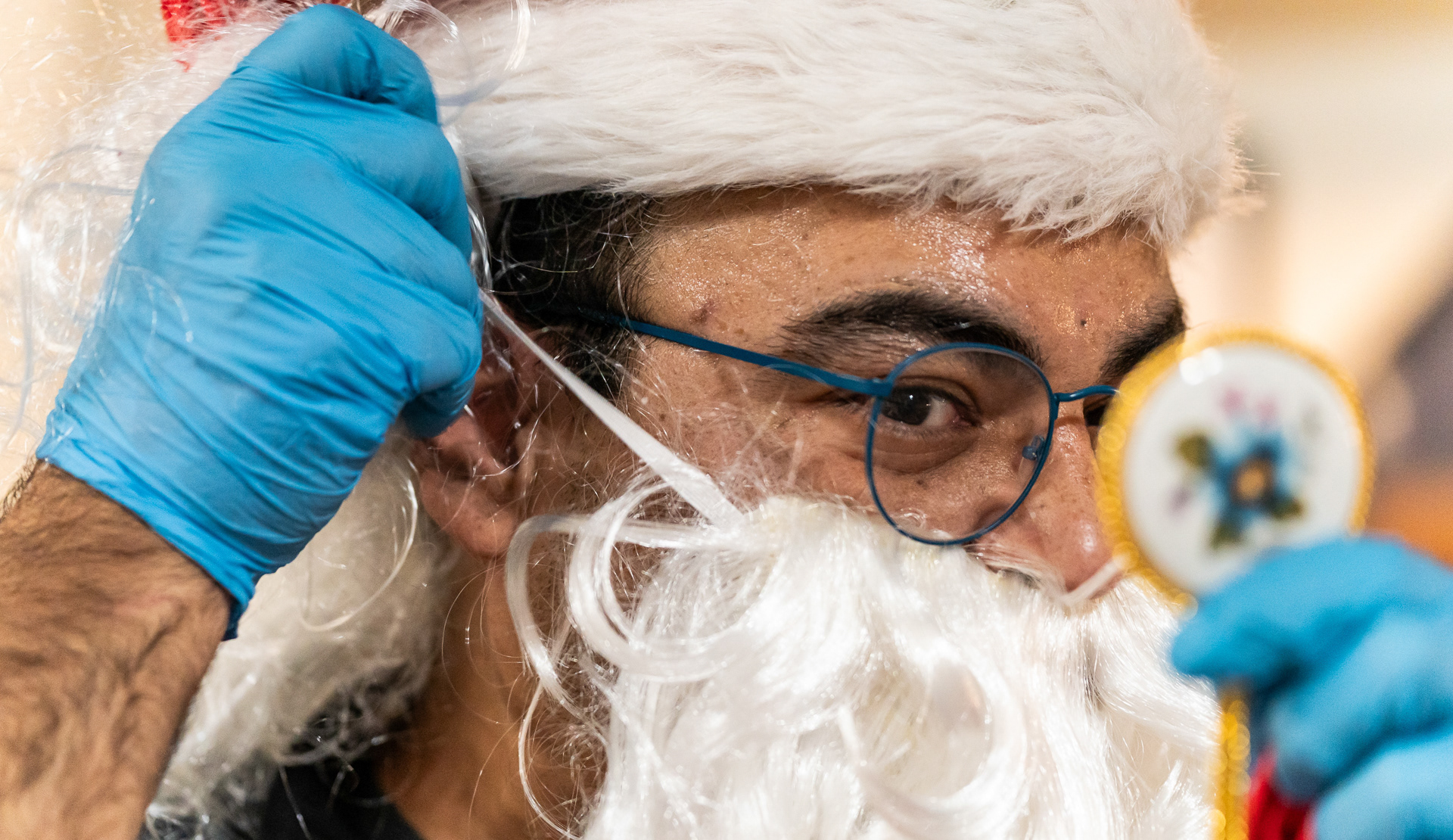 Daniel Cano se mira con un espejo pequeño mientras se pone una barba falsa en el puesto 974 de la American Legion en Franklin Park, Illinois el 17 de noviembre, 2023.