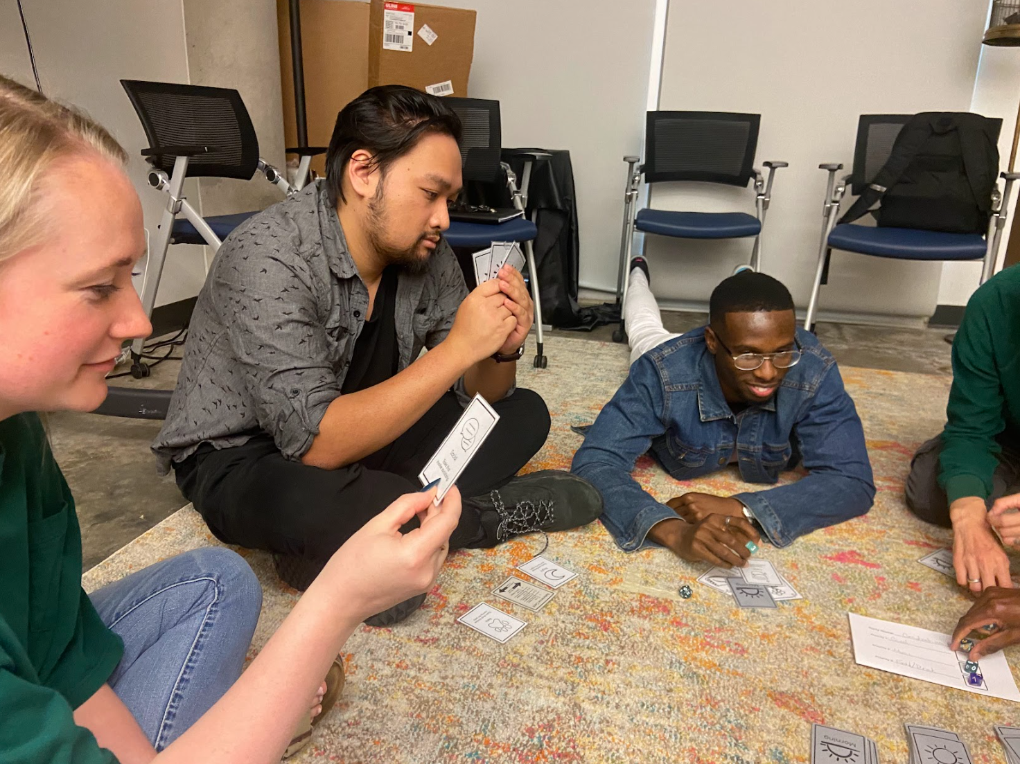 Three players sit on a rug with game cards in their hand.