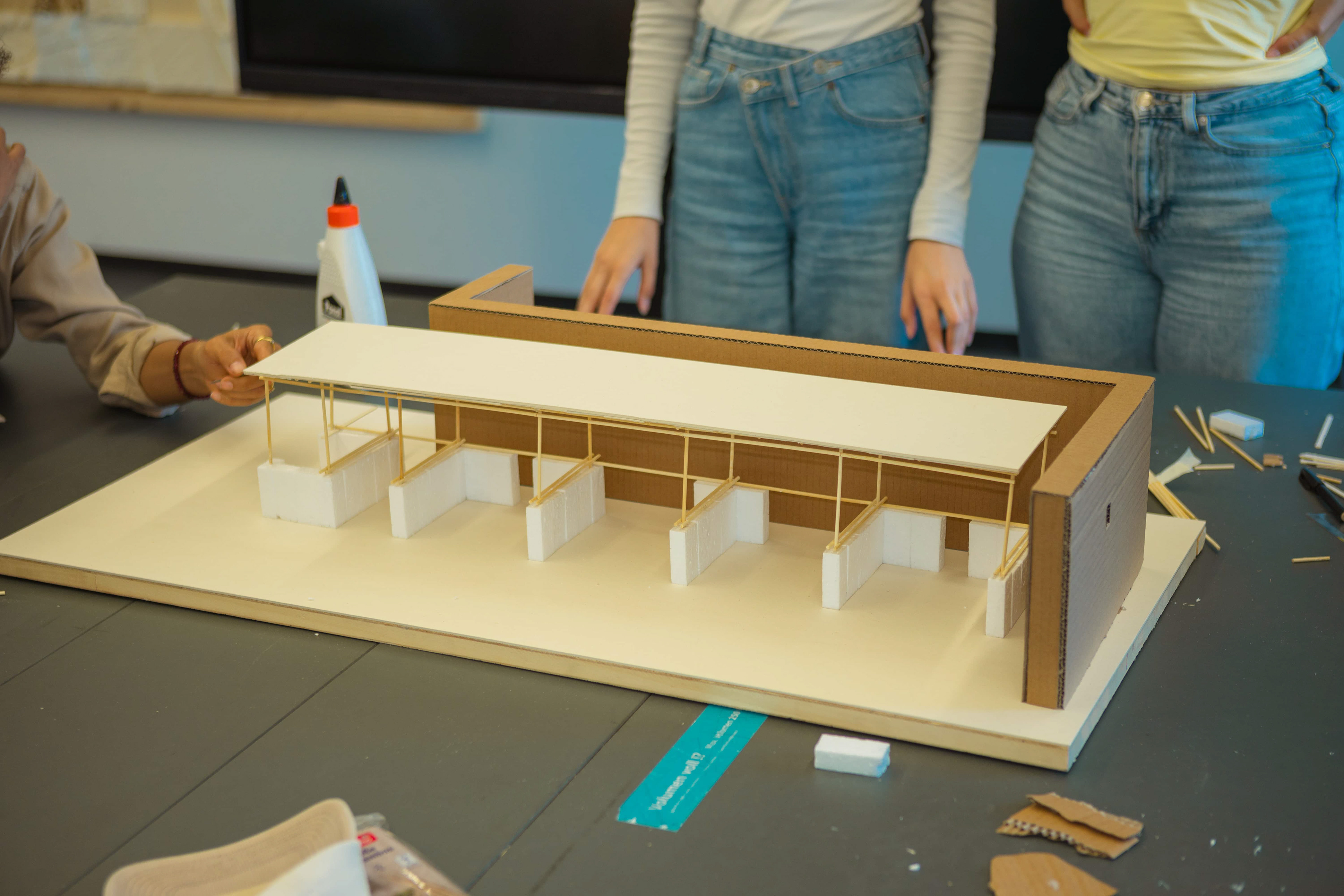 Entwurfsmodell Pavillon Ehrenfeld – Pappmodell mit Holzstäben als Gerüst, Gabionensockel aus Styropor, Kontext Bestandsgebäude, Bausituation im Seminar