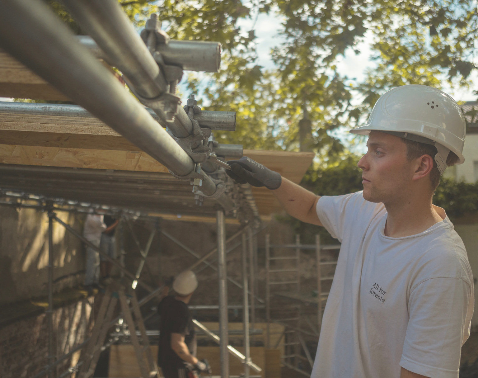 Bauphase Pavillon Ehrenfeld – Student befestigt Gerüstkupplungen an der Holzunterkonstruktion, im Hintergrund weitere Studierende bei der Montage