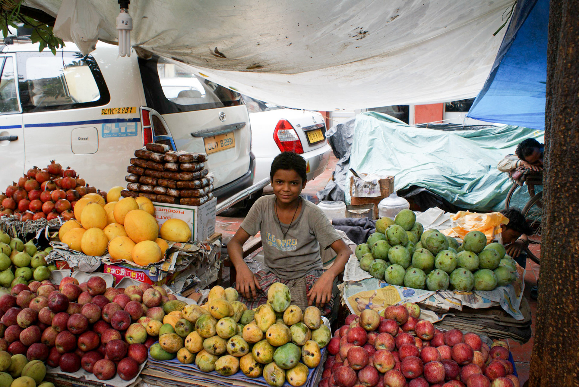Kid covering for fruit stall in Delhi while father takes a sleep break