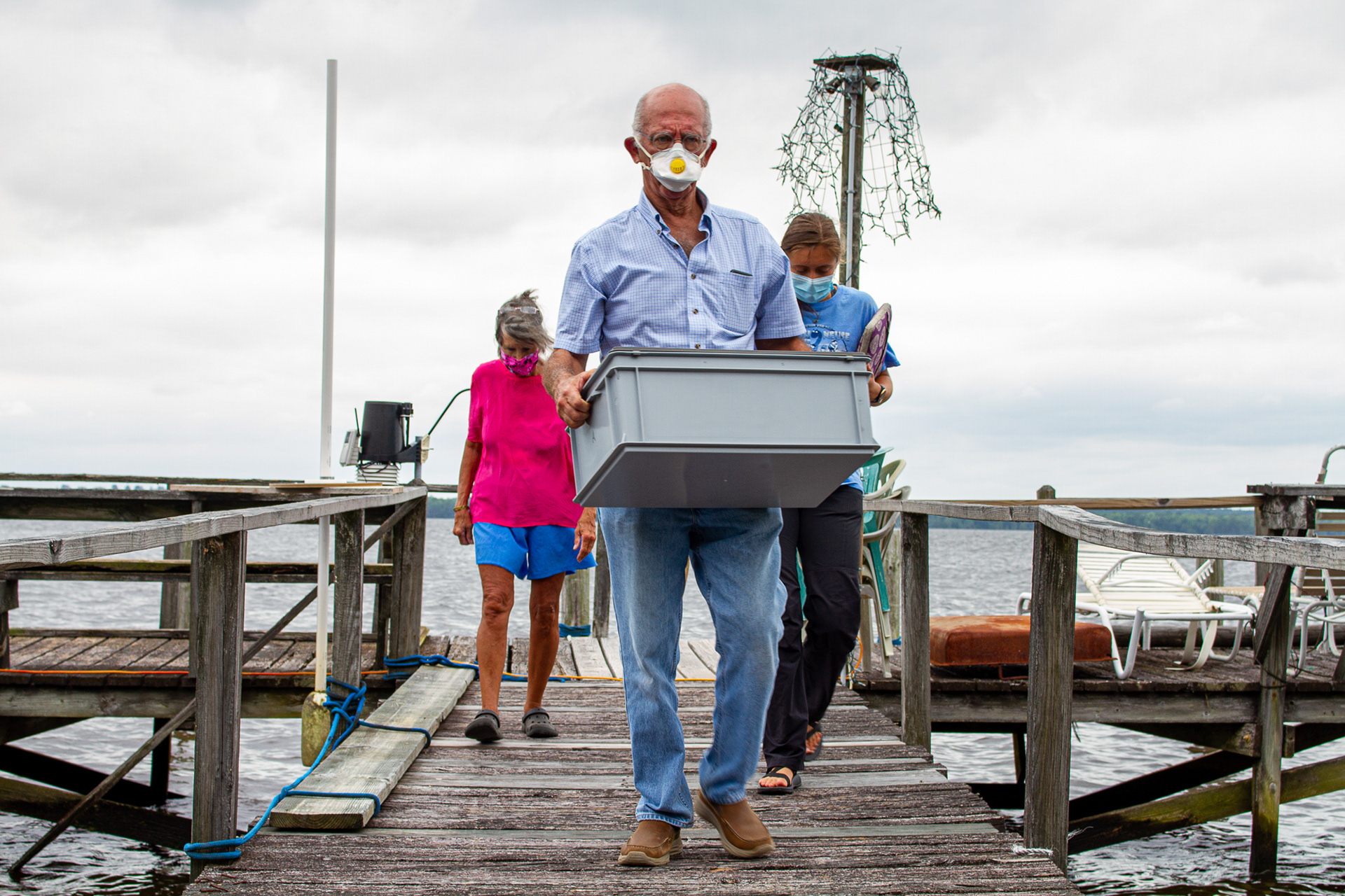 Manu Suarez, a volunteer with the Chowan-Edenton Environmental Group (CEEG), carries supplies from a research station near Edenton, N.C., June 11, 2020. While masks were required due to the coronavirus pandemic, volunteers studying cyanobacteria have been wearing masks for years to avoid inhaling toxins in the air.