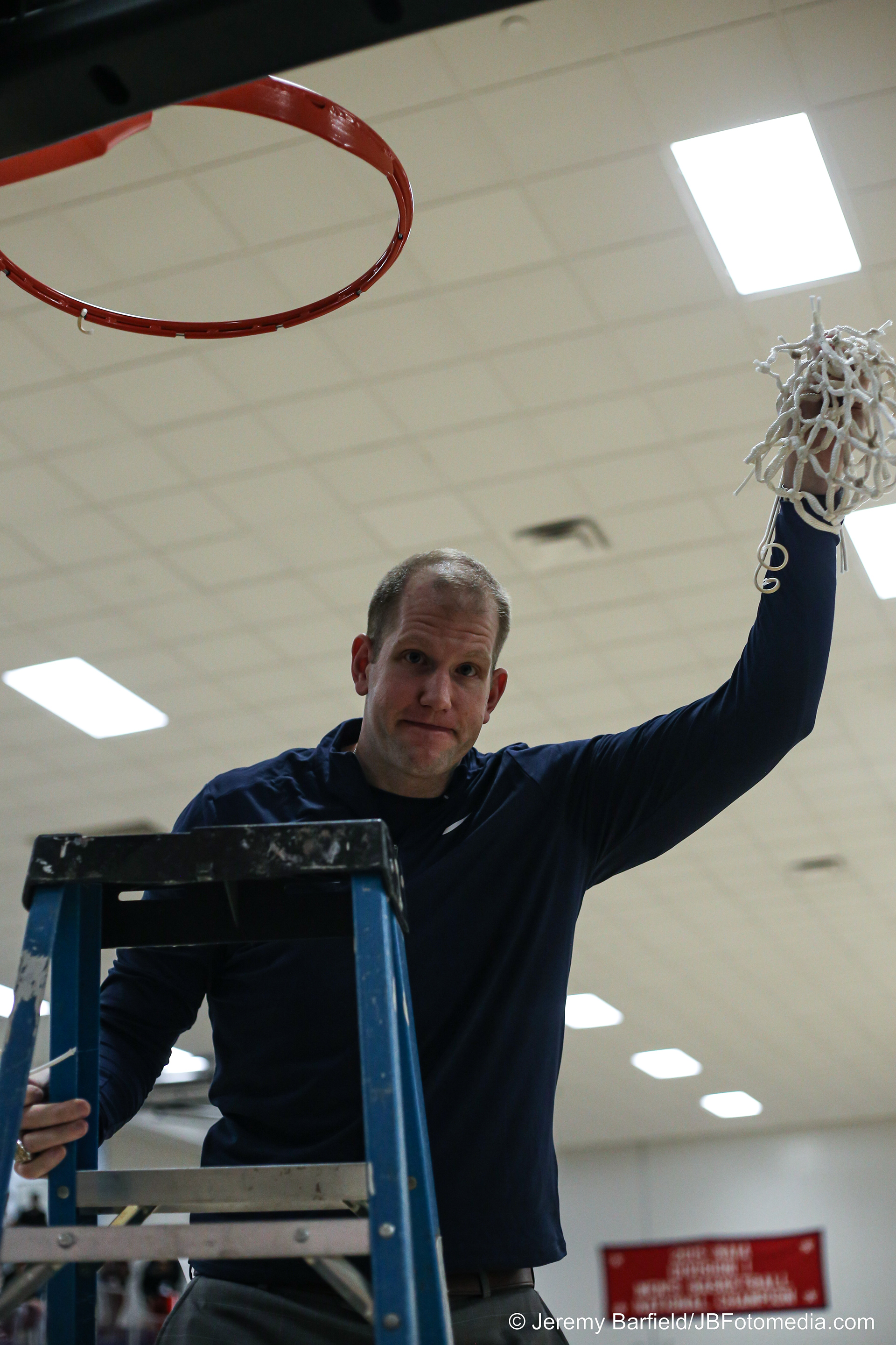 Coach Alex Ireland cutting down the basketball net after the team won the Souther States Athletics Conference regular season championship in the 2024-25 season