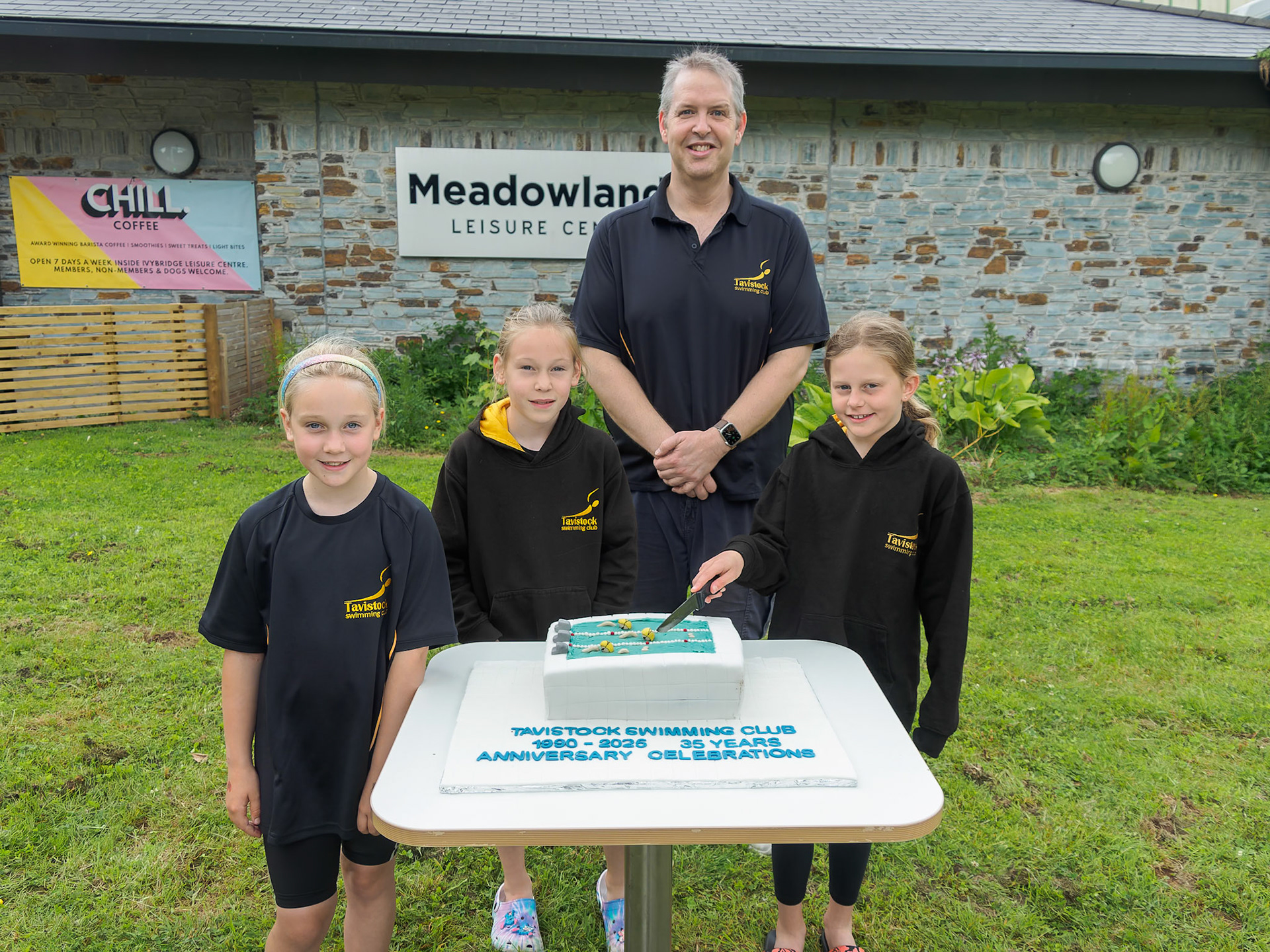 Three young swimmers and head coach, with celebration cake made by Karen Ball