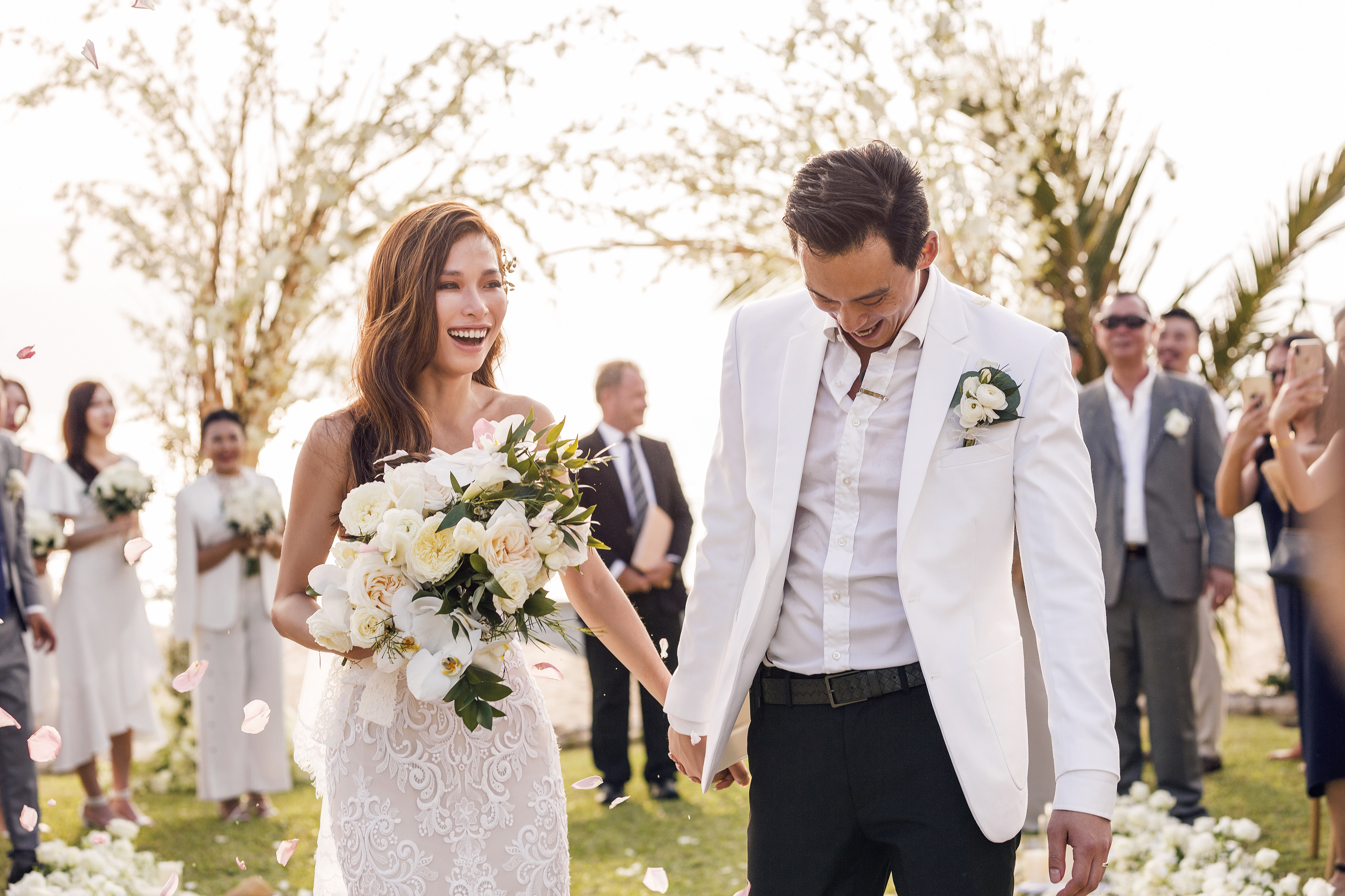 Bride with a flower bouquet and groom walks down the aisle while family and friends applaud 