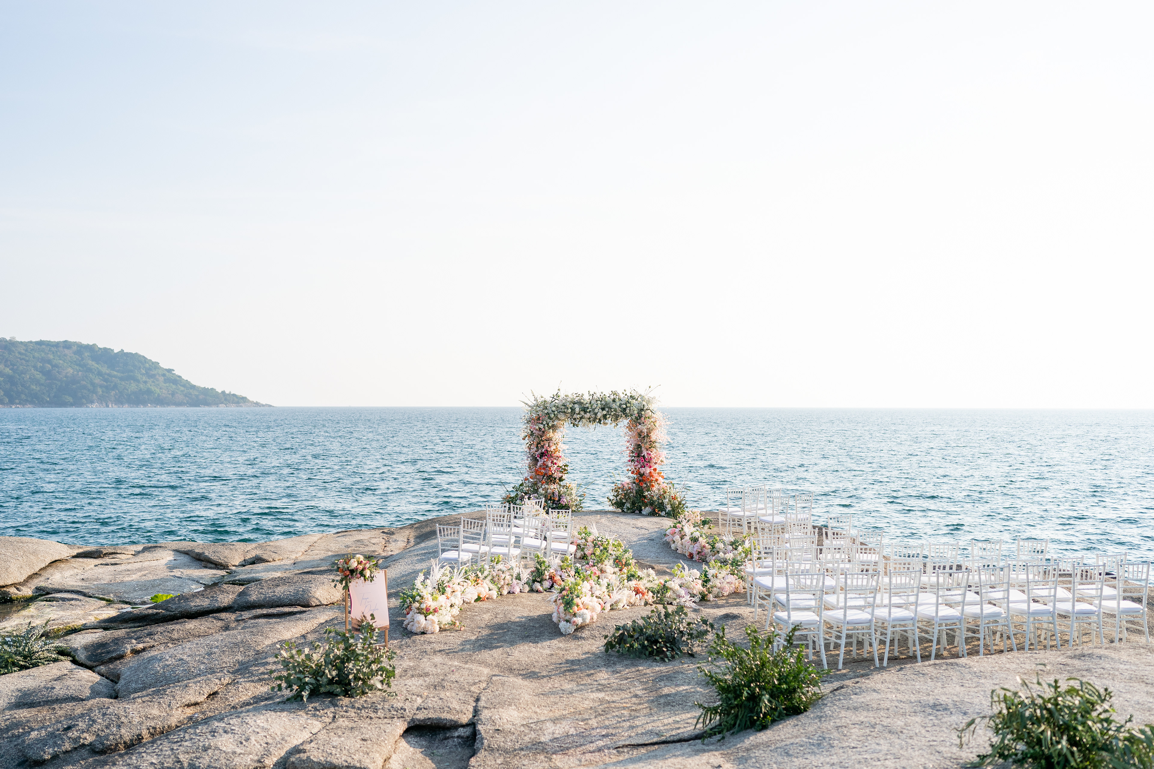 Wedding ceremony setup with flower arch and white chairs at Kata Rocks upon the Andaman Sea. Phuket Krabi Samui Phang nga Thailand wedding photographer photographing wedding photography of a beautiful beach wedding in Phuket