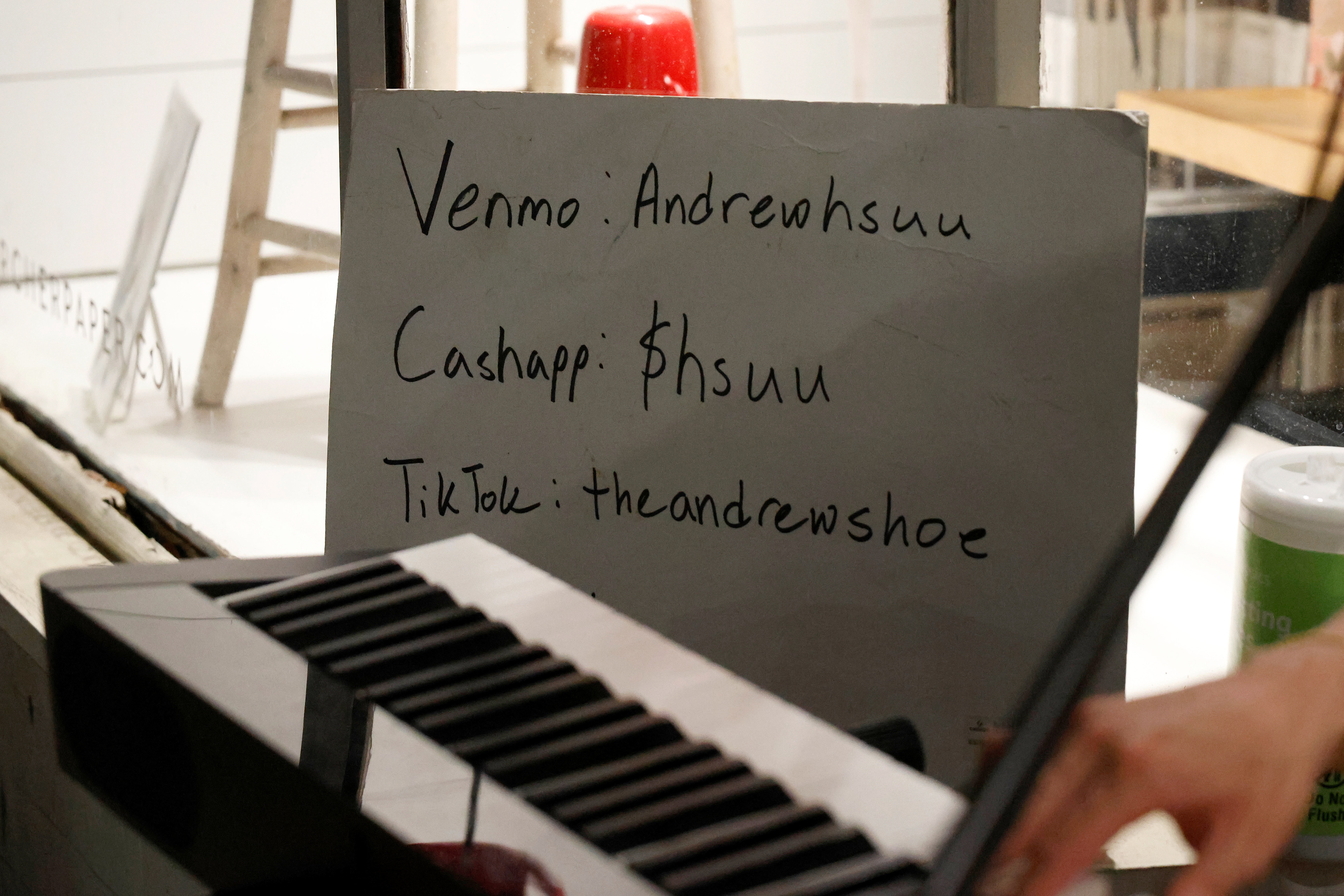 A sign sits out next to Andrew Hsu for spectators to donate while he performs in downtown Athens, Georgia, on Thursday, April 3, 2025. Hsu also has a bucket to collect cash donations that sits at his feet.
