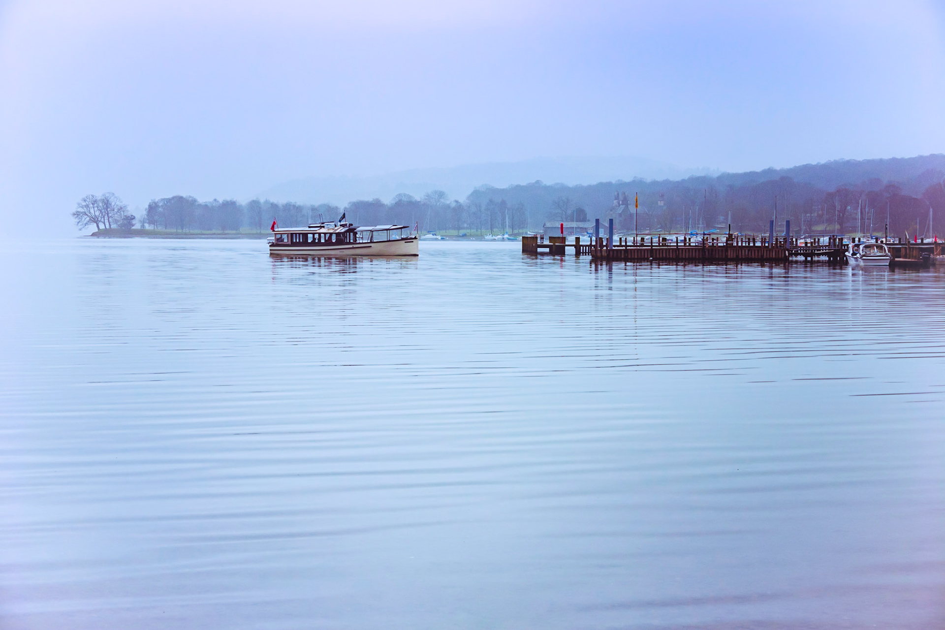A toned image of the Ullswater lake ferry arriving at Pooley Bridge landing on a quintessentially quiet moody morning in the English Lake District National Park.