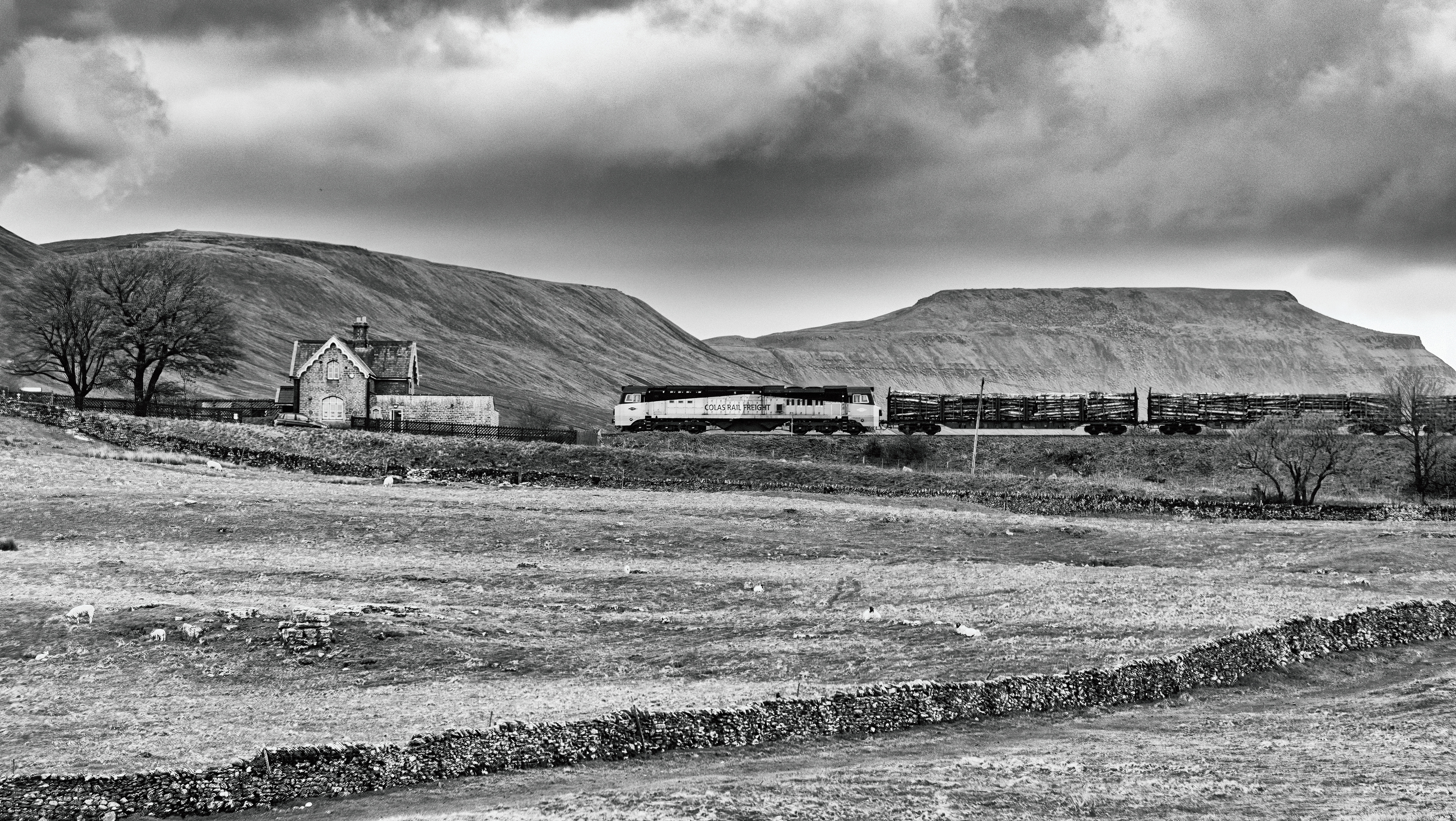 Mono image - Colas Class 70 passing Ribblehead station with Ingleborough in the background