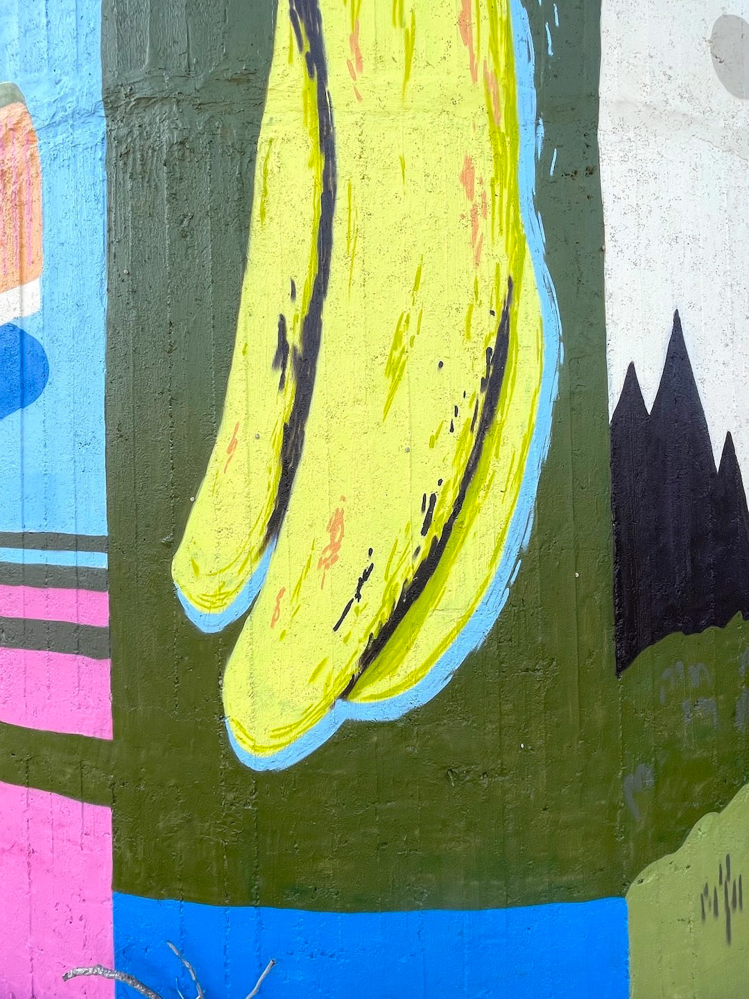 A mural painted on a wall depicts two yellow bananas with black outlines on a colorful abstract background.