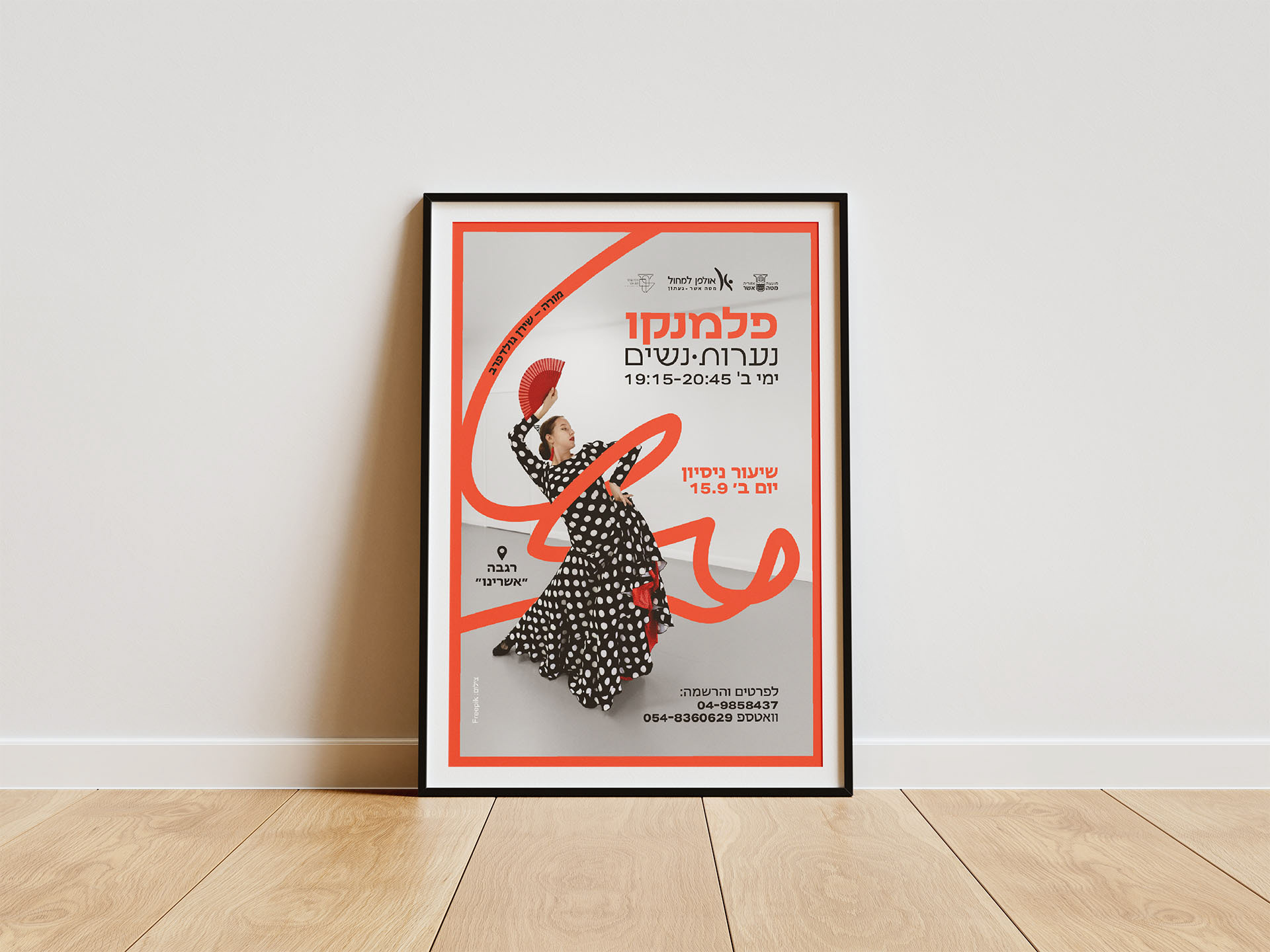 Framed poster on wooden floor against white wall, featuring a dancer in a black and white polka dot dress with a fan, surrounded by red script. Text in Hebrew.