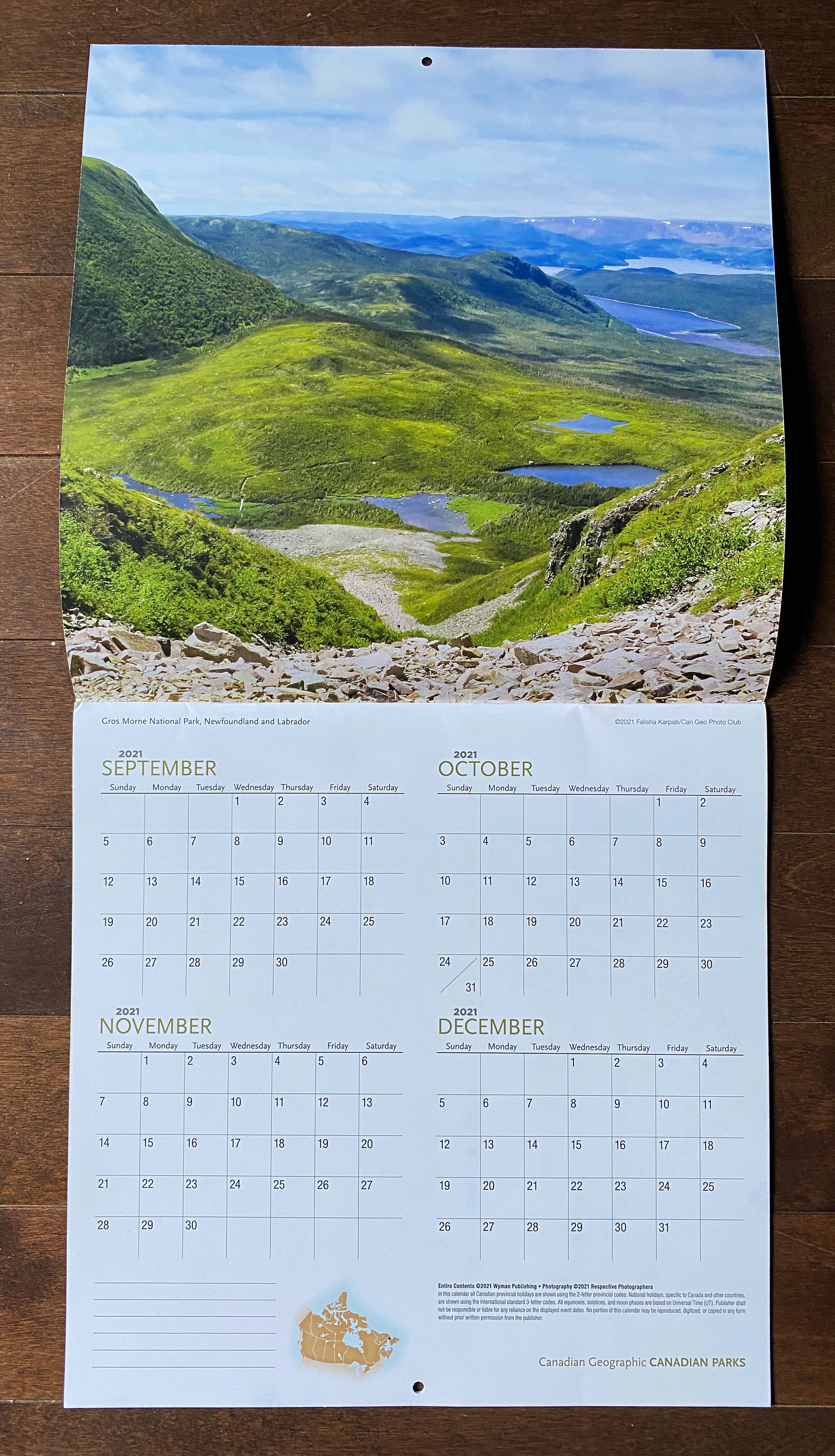 Calendar open to a page showing the last 4 months of 2021 on the bottom, and on the top is Falisha's photo of Gros Morne Mountain with a green hilly landscapes mixed with bodies of water.