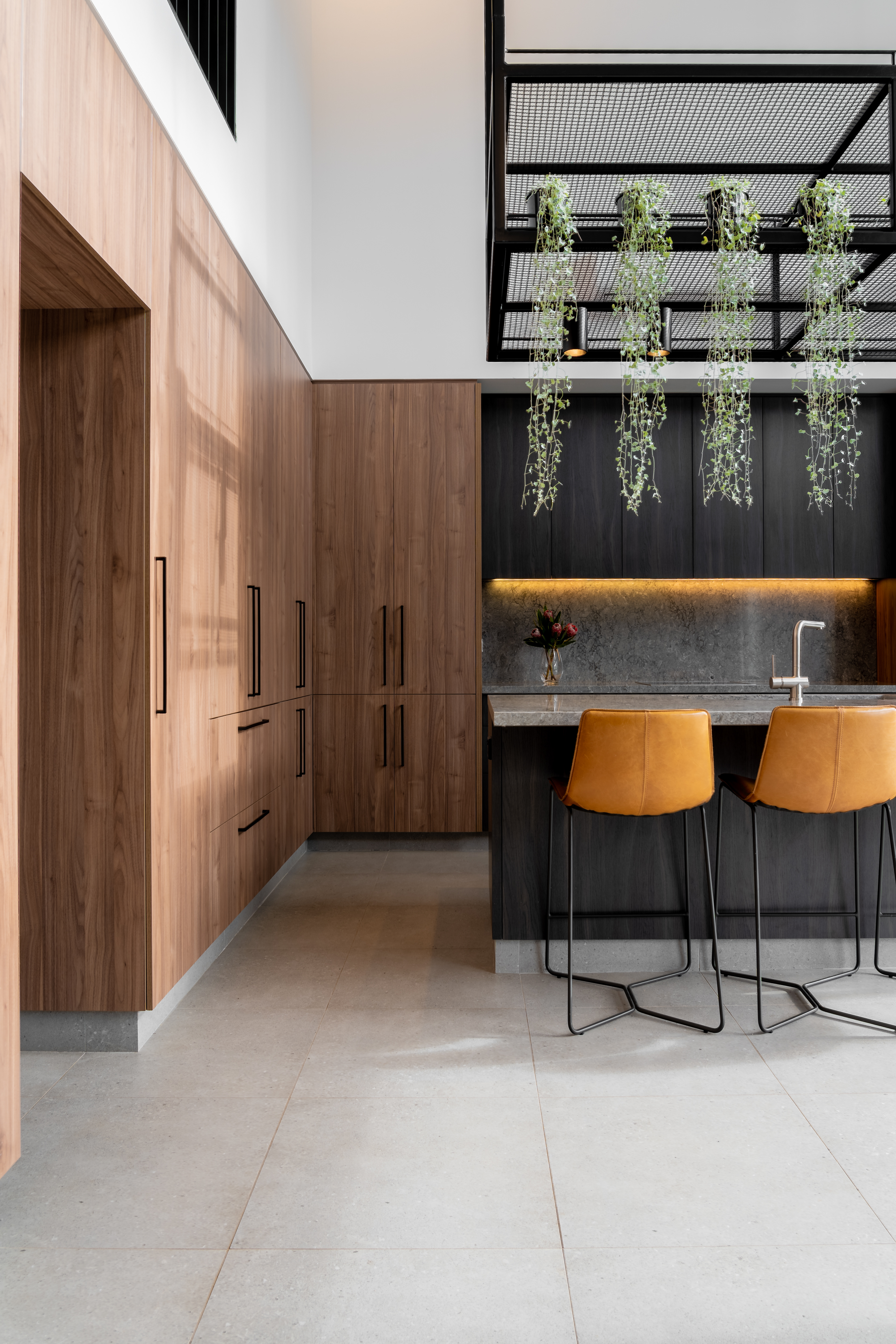 New modern contemporary kitchen with seamlessly integrated appliances, contrasting cabinetry and custom designed metalwork hangar suspended over an engineered stone benchtop.