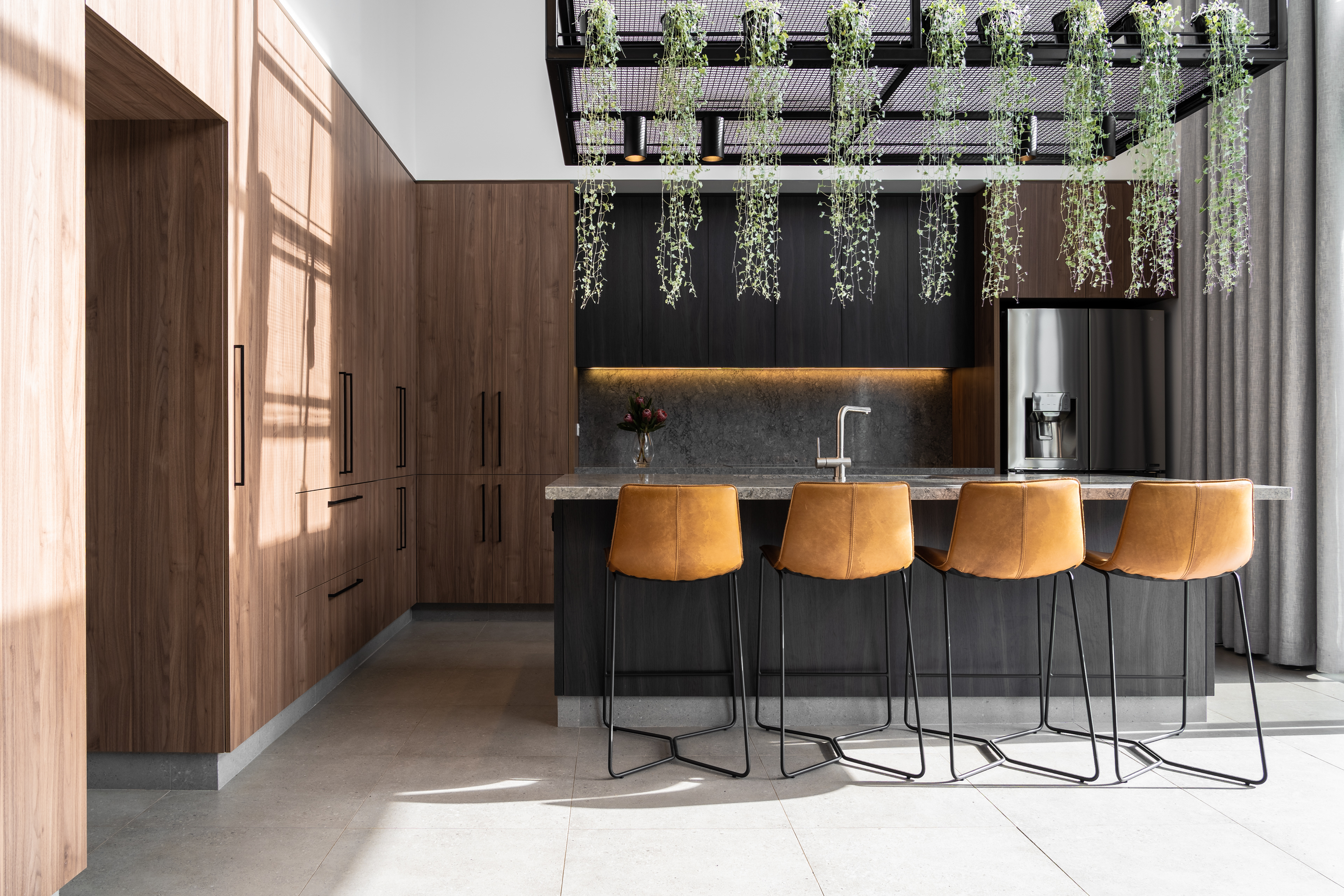 New modern contemporary kitchen with seamlessly integrated appliances, contrasting cabinetry and custom designed metalwork hangar suspended over an engineered stone benchtop.