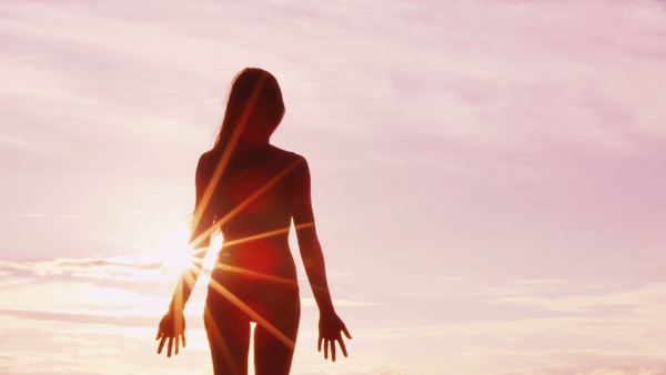 silhouette of a woman standing at the beach at sunset raising her hands above her head