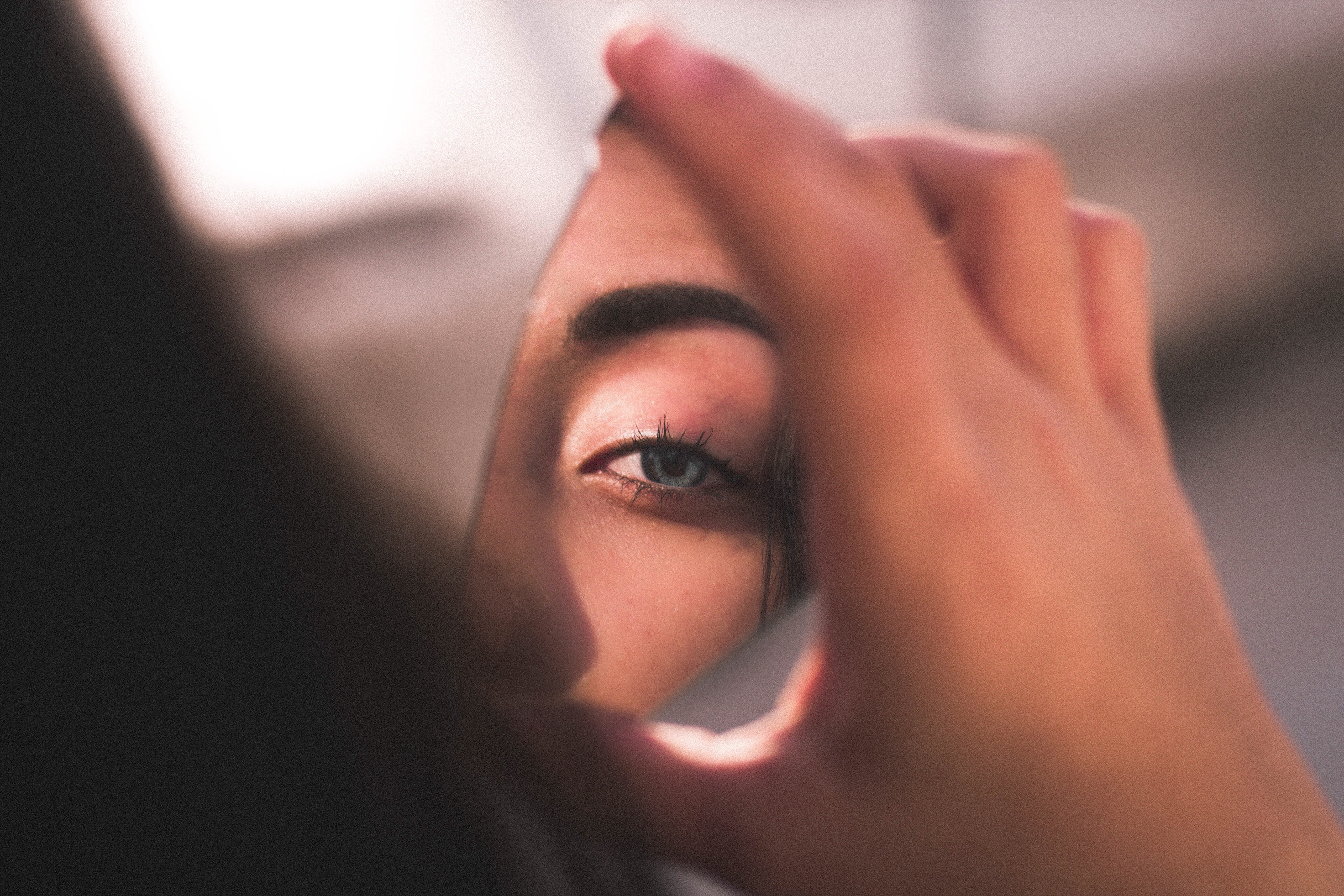 a person's hand holding a reflection of a woman's eye and eyebrow in a fragment of a mirror
