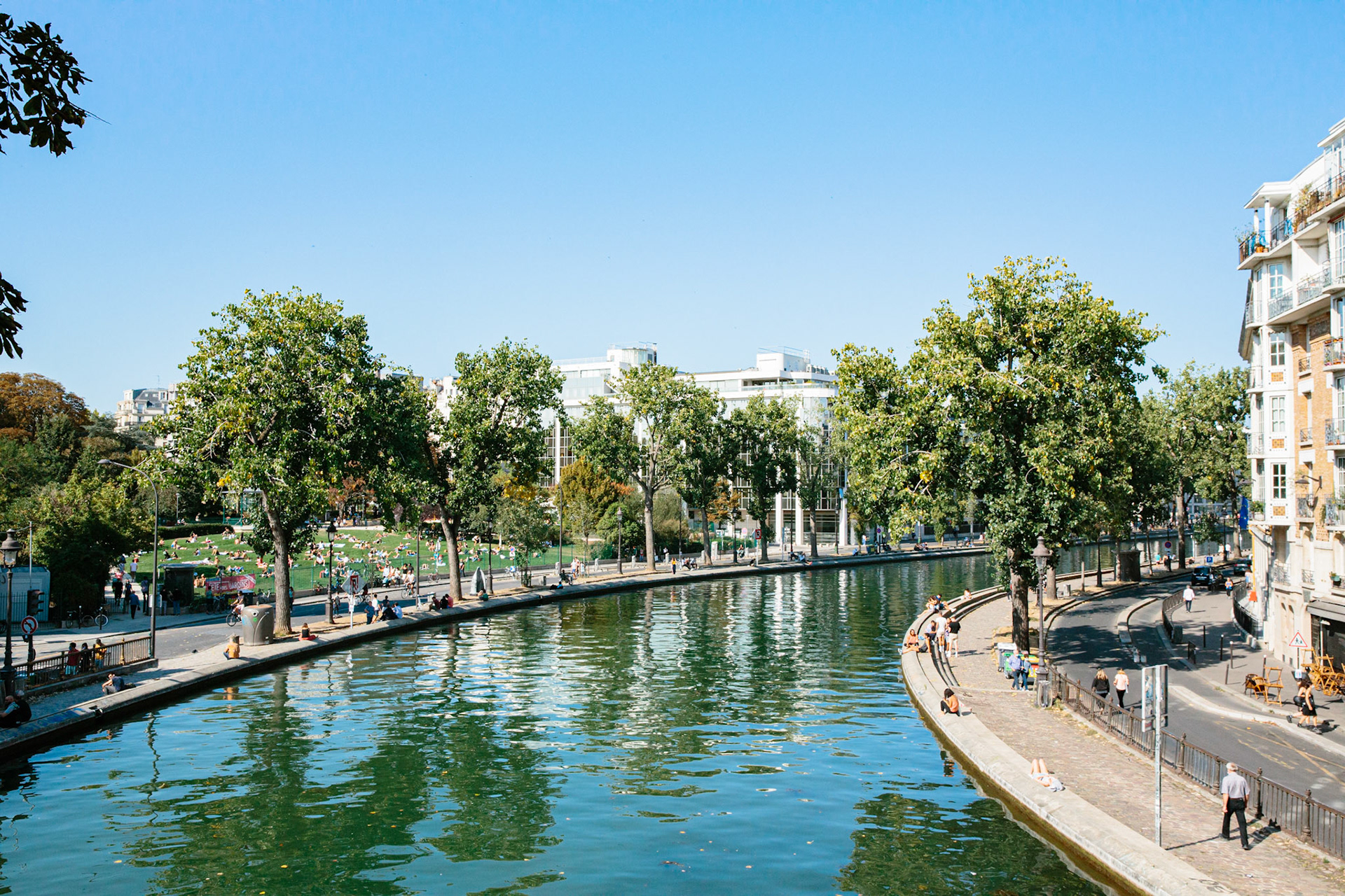 Passées les écluses, le canal fait une courbe et continue de remonter. On aperçoit sur l’autre rive à gauche la pelouse du jardin villemin.