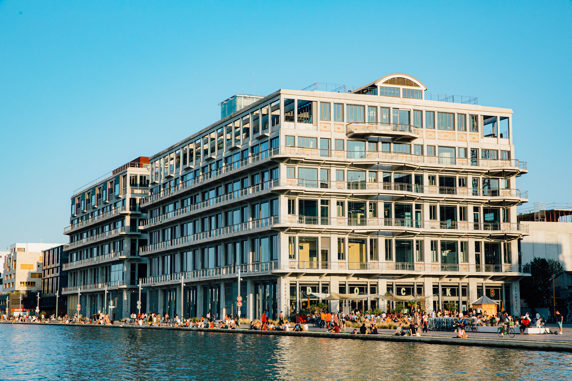 Il y a foule. Les magasins généraux étaient des entrepots industriels pendant tout le XXe siècle. Le batiment est resté inoccupé de 1995 à 2012. Quand j’étais à vélo, enfant, sans en connaître l’histoire, c’était un repère visuel emblématique à Pantin, je savais que je m’approchais de Paris. Les graphitis multicolores ont laissé place à une splendide façade monochrome, et la vie nocturne ressemble à s’y méprendre à Paris.