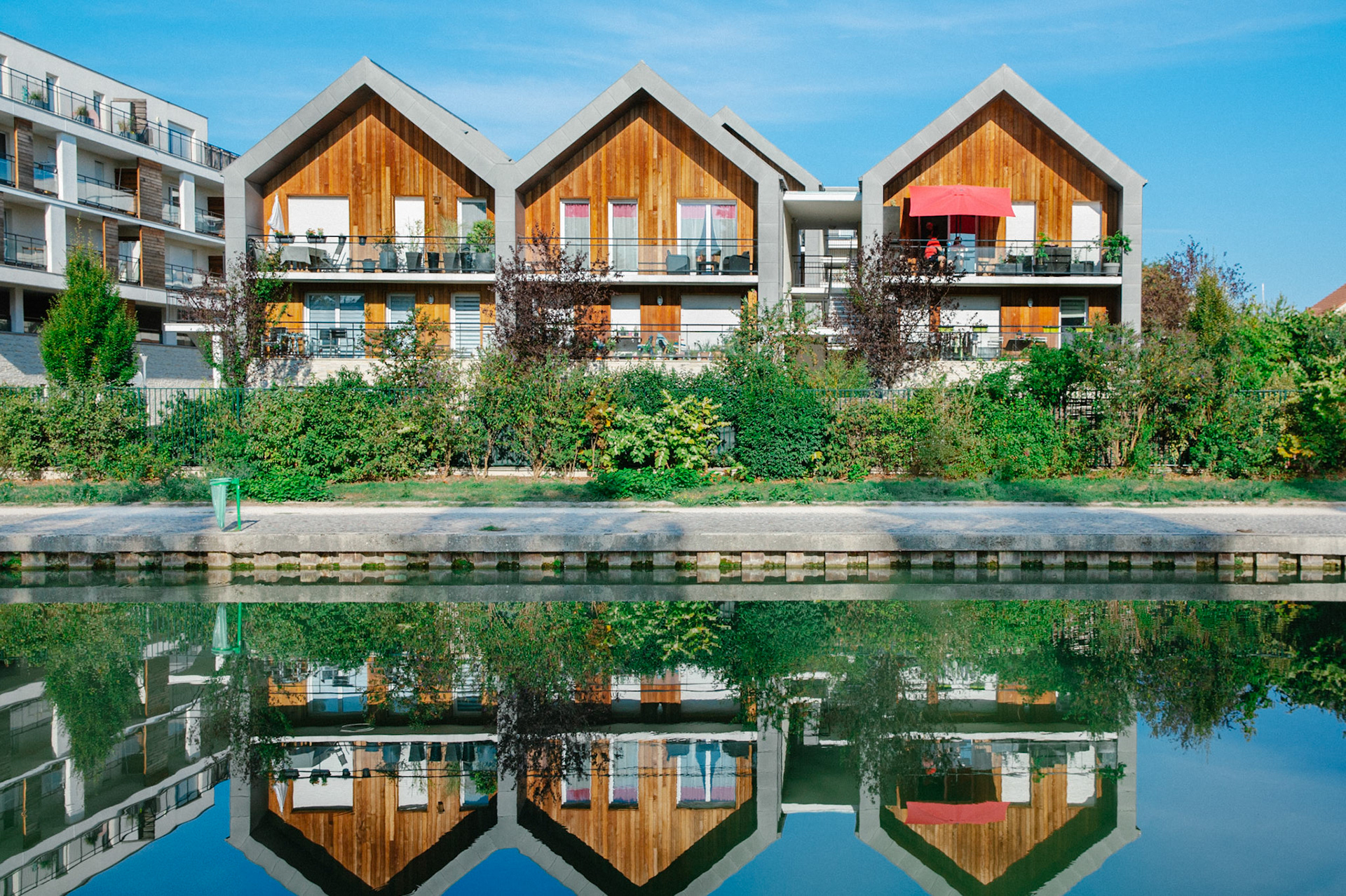 10h du matin, le soleil s’élève à l’horizon, et illumine ces trois maisons dont le reflet donne une impression magique sur le canal de l’Ourcq. Sur leur balcon, à l’ombre sous un parasol, une famille prend son petit-déjeuner.