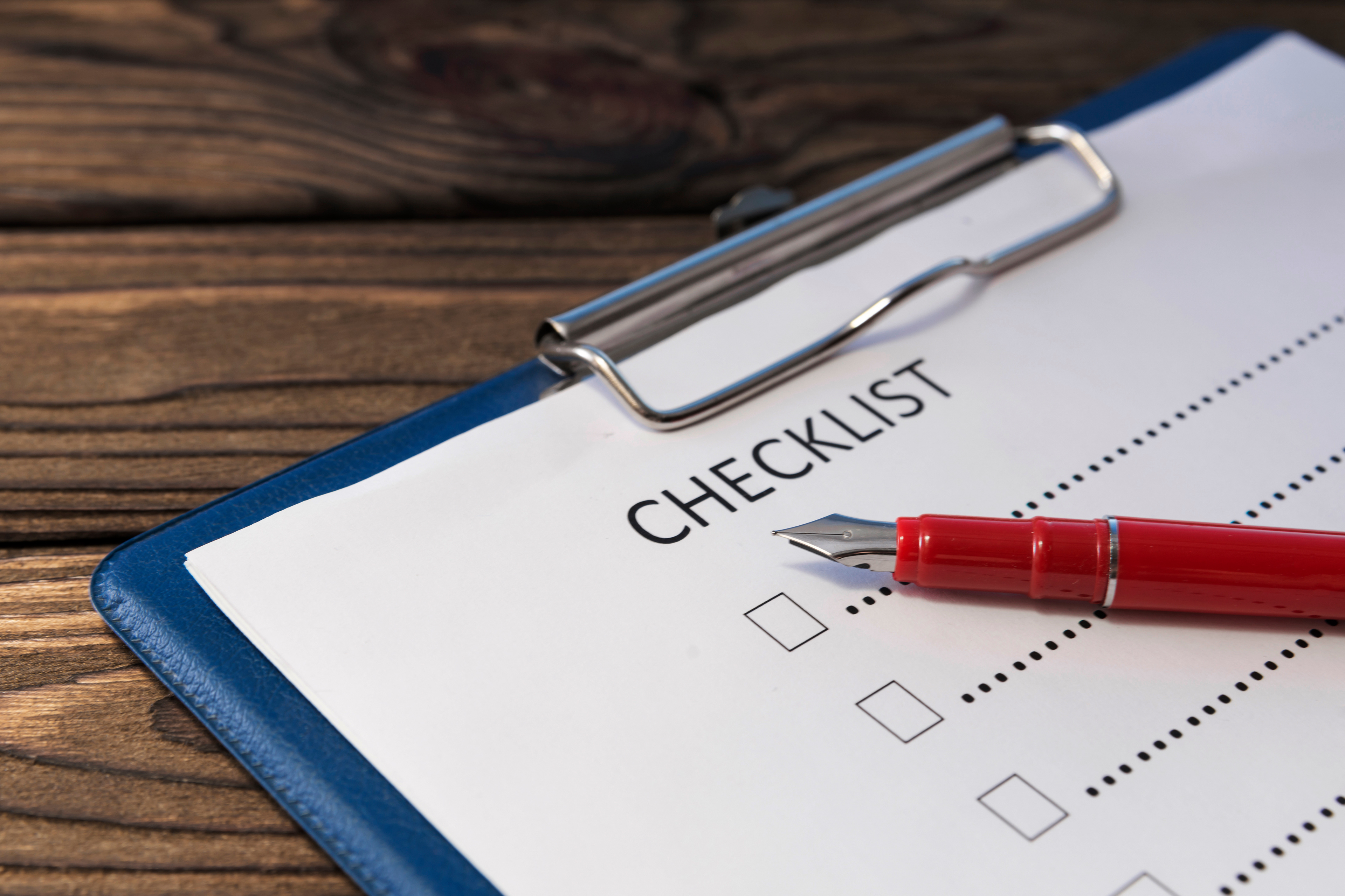 Close-up photo of a paper checklist on a clipboard with a red fountain pen laying across it.