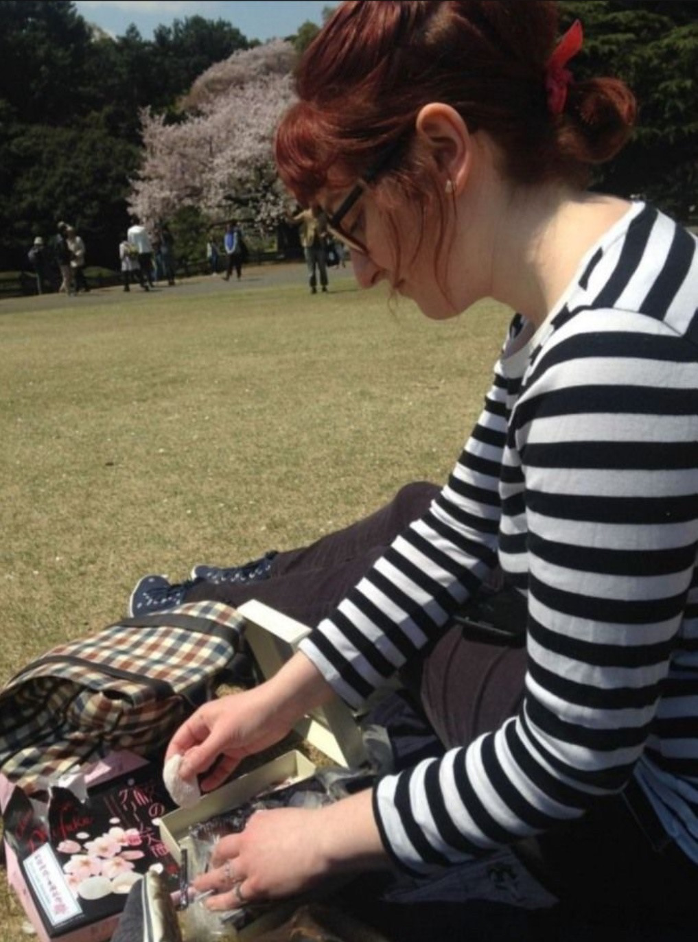 Photo of Nora sitting in a field with cherry blossom trees in the background.